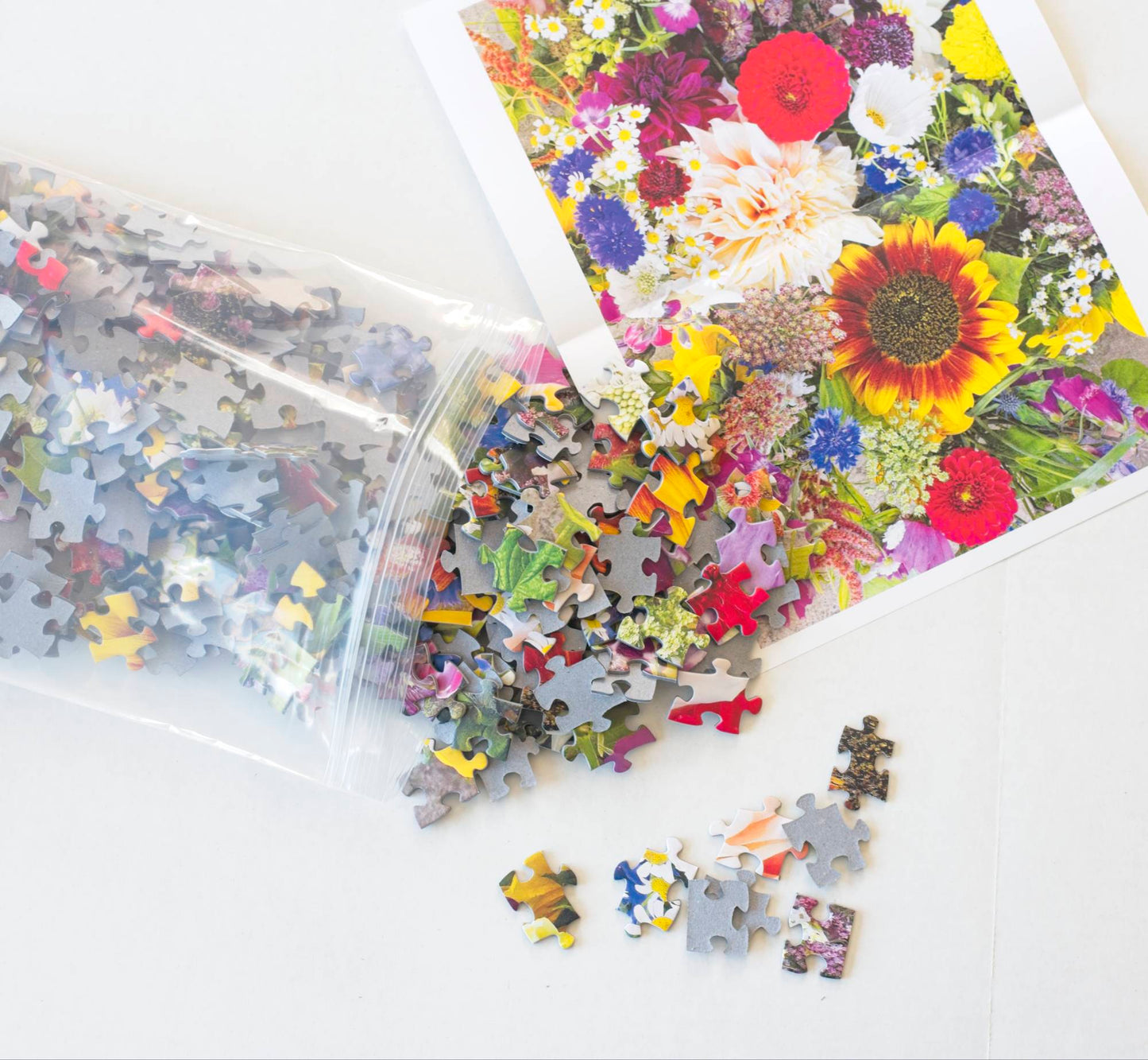 A floral puzzle spilling out of a resealable bag onto a white surface with a reference poster laying next to it.