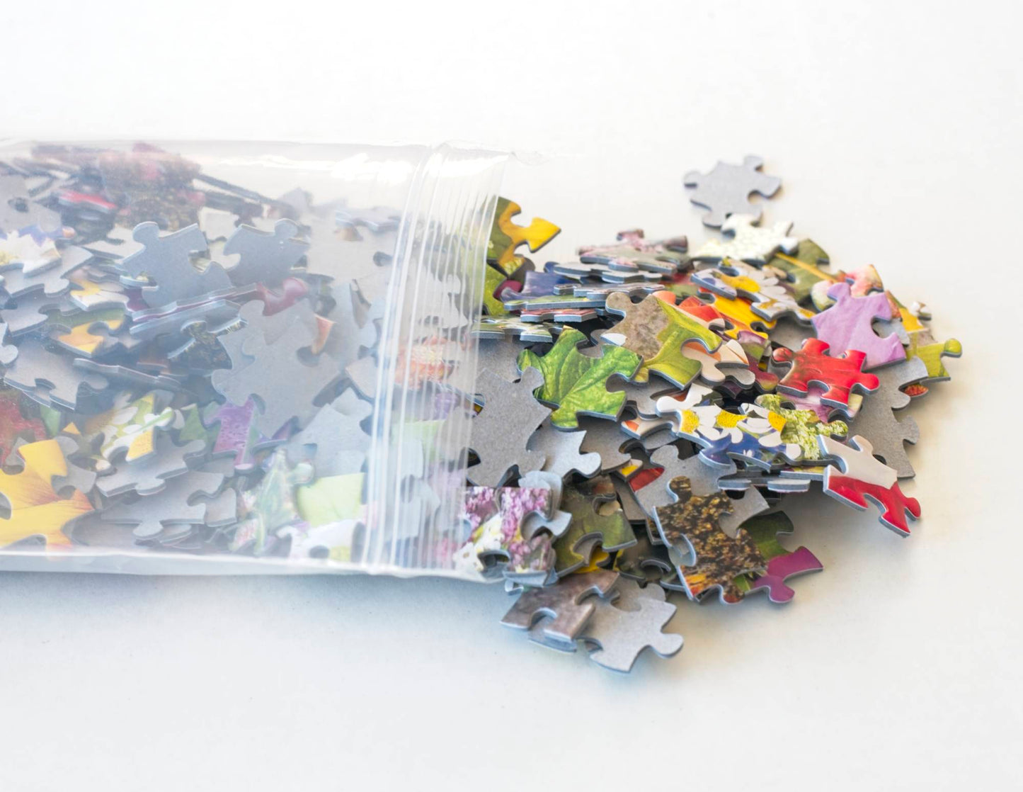 A photograph of colorful floral jigsaw puzzle pieces spilling out onto a white surface.