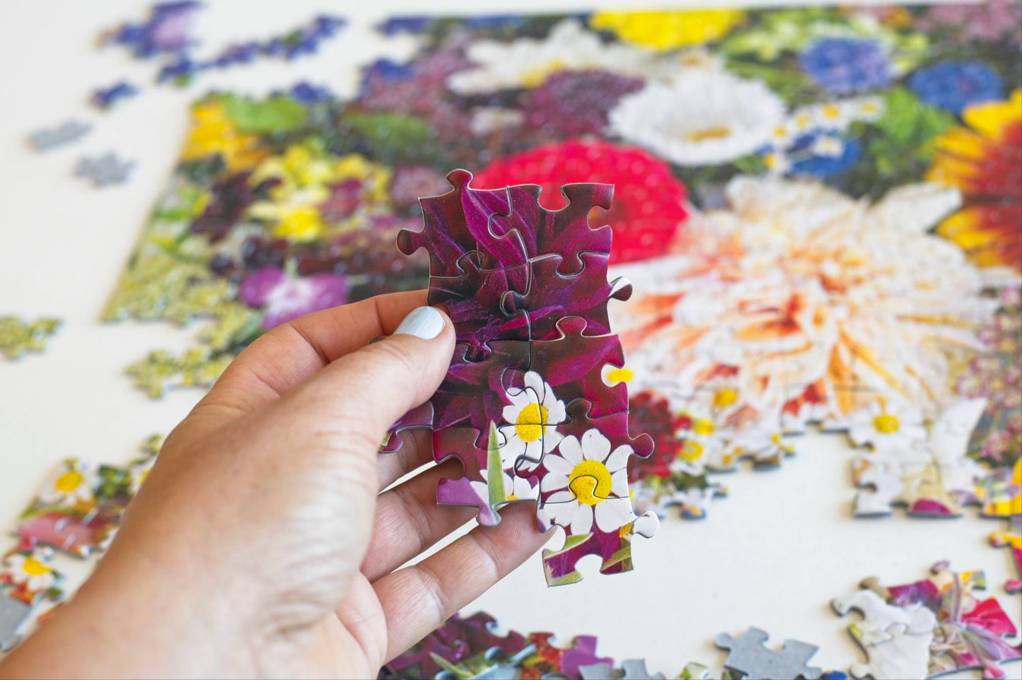 Hand holding a completed section of a completed jigsaw puzzle with a large section blurred in the background