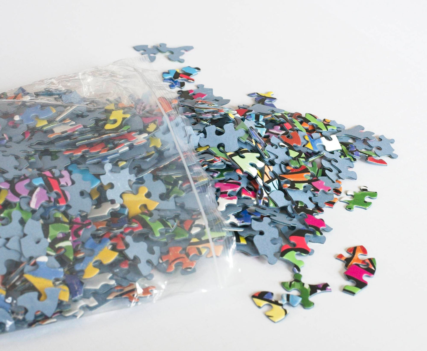 brightly colored random-cut puzzle pieces made from blue board spill out of a resealable plastic bag.