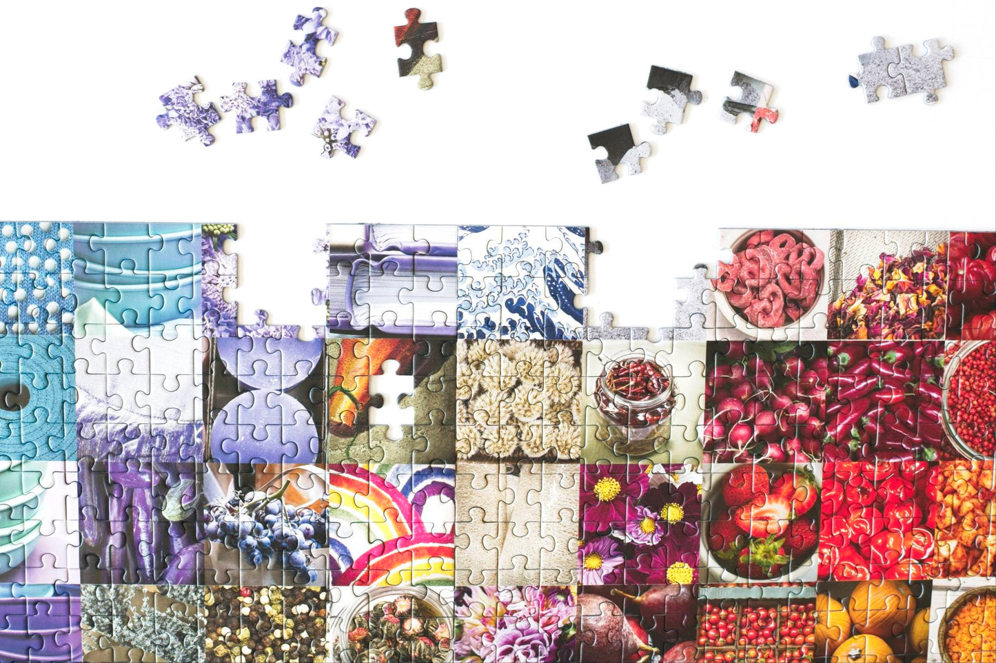A top section of a nearly complete jigsaw puzzle with a few pieces scattered above. The puzzle has photos of colorful geometric patterns and items in a grid pattern.