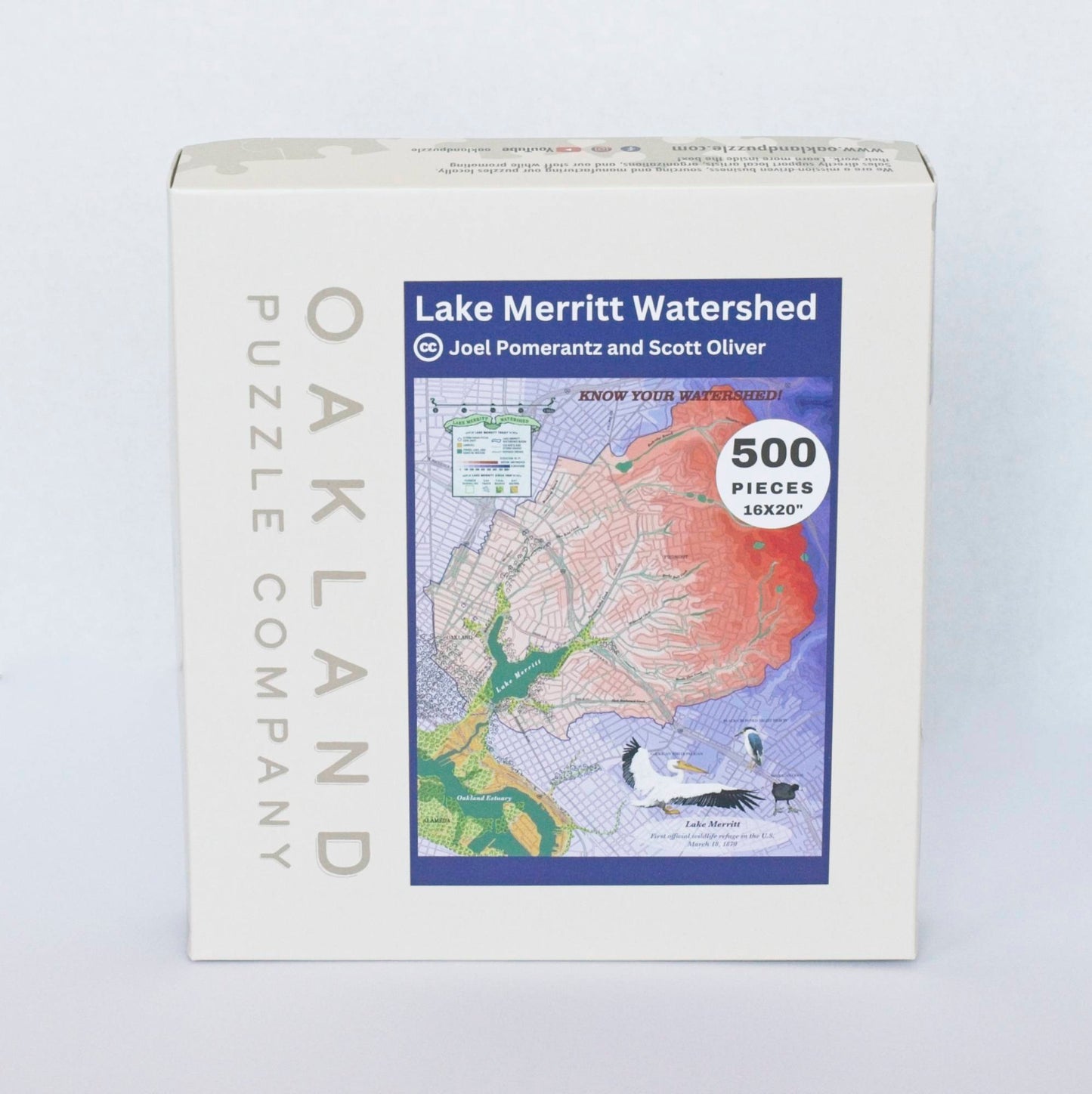 A box branded Oakland Puzzle Company with a label featuring a colorful topographic map centered around a lake and estuary reading Lake Merritt Watershed by Joel Pomerantz and Scott Oliver