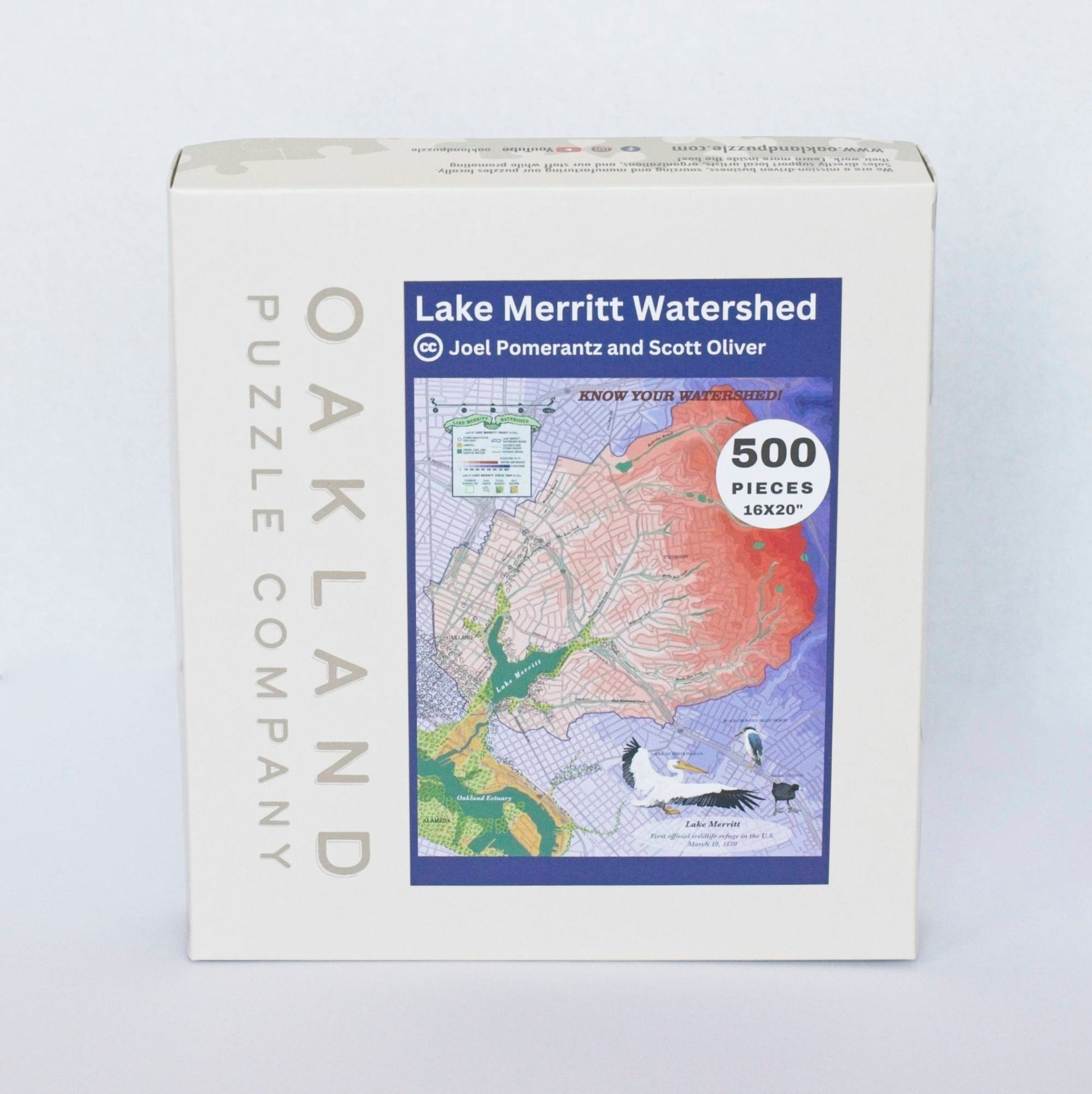A box branded Oakland Puzzle Company with a label featuring a colorful topographic map centered around a lake and estuary reading Lake Merritt Watershed by Joel Pomerantz and Scott Oliver