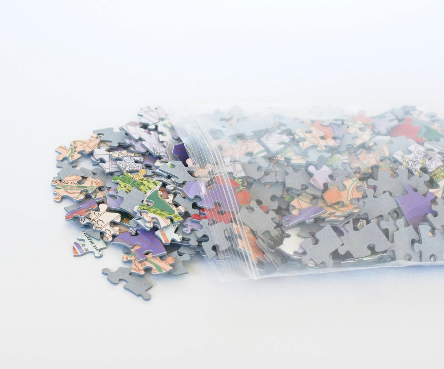 A resealable plastic bag with colorful random cut puzzle pieces spilling from it.