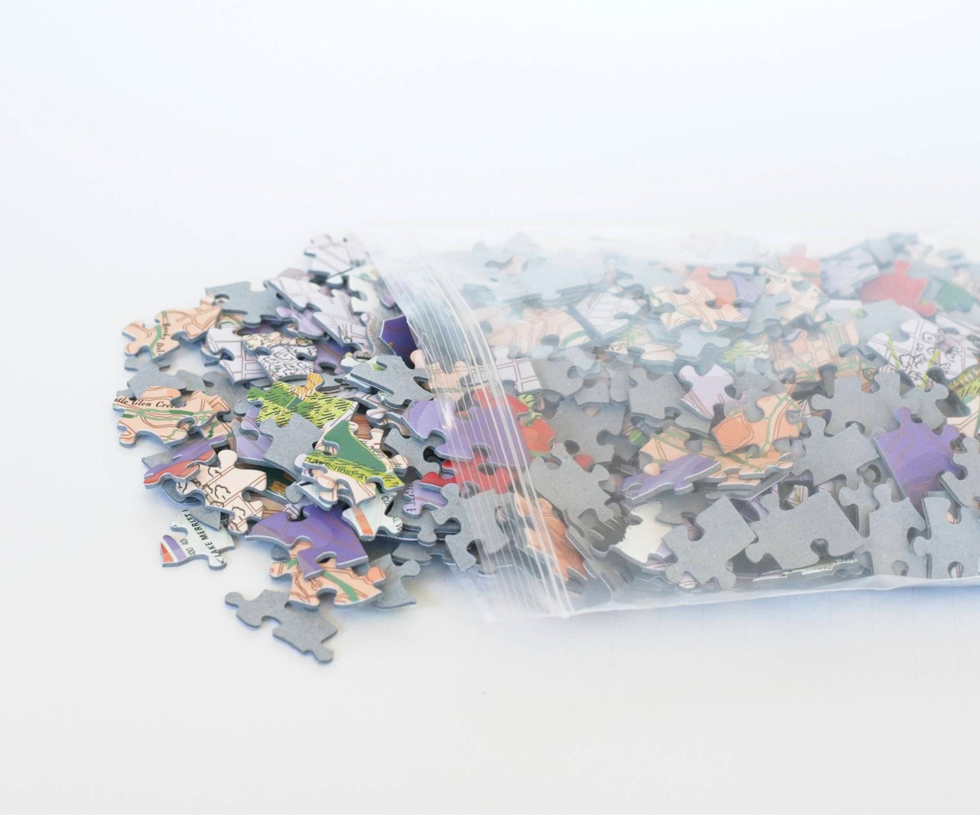A resealable plastic bag with colorful random cut puzzle pieces spilling from it.