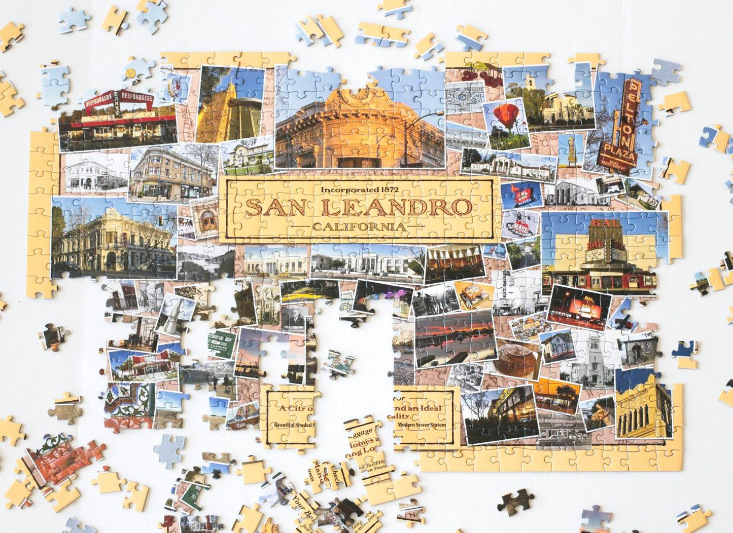 A nearly completed jigsaw puzzle with landscape, architecture, and art detail photos collaged on a yellow background with the text "Incorporated 1872 San Leandro California" prominent in the center. Remaining pieces and partially completed sections are scattered around.