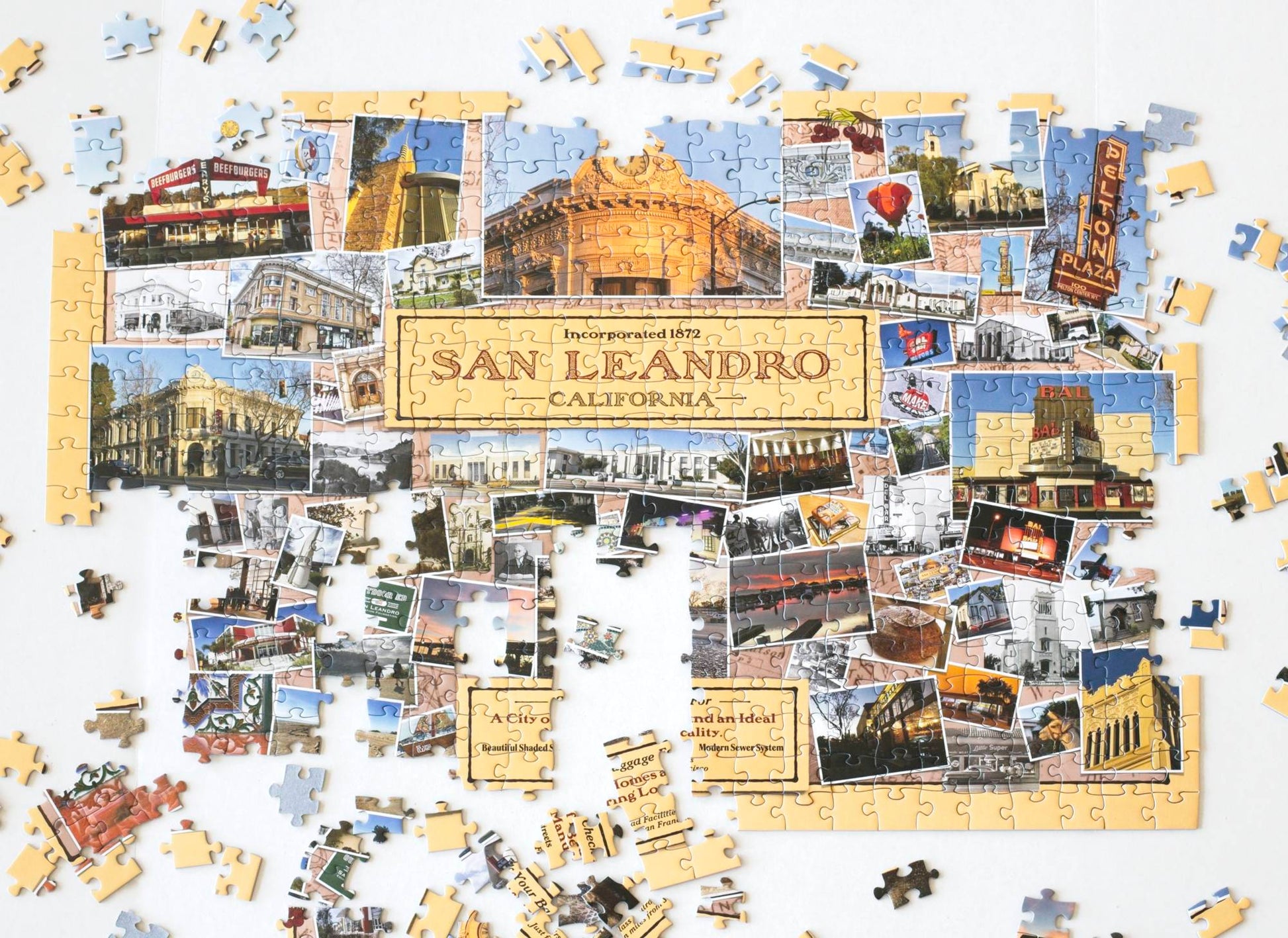 A nearly completed jigsaw puzzle with landscape, architecture, and art detail photos collaged on a yellow background with the text "Incorporated 1872 San Leandro California" prominent in the center. Remaining pieces and partially completed sections are scattered around.