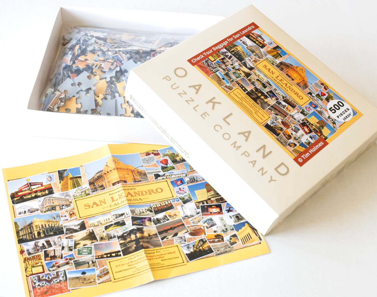 An photo of a jigsaw puzzle box with the lid off and askew from the box bottom which contains a plastic bag with jigsaw puzzle pieces. Next to it lies a poster that matches the puzzle image on the front of the box.