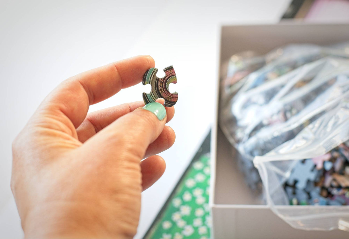 Hand holding a puzzle piece with a blurred background of a box of similar pieces.