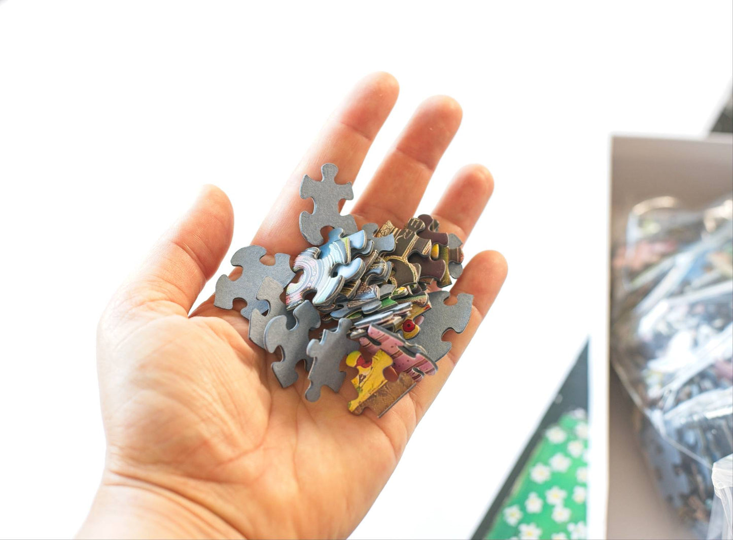 Hand holding a collection of puzzle pieces with colorful designs on a blurred background