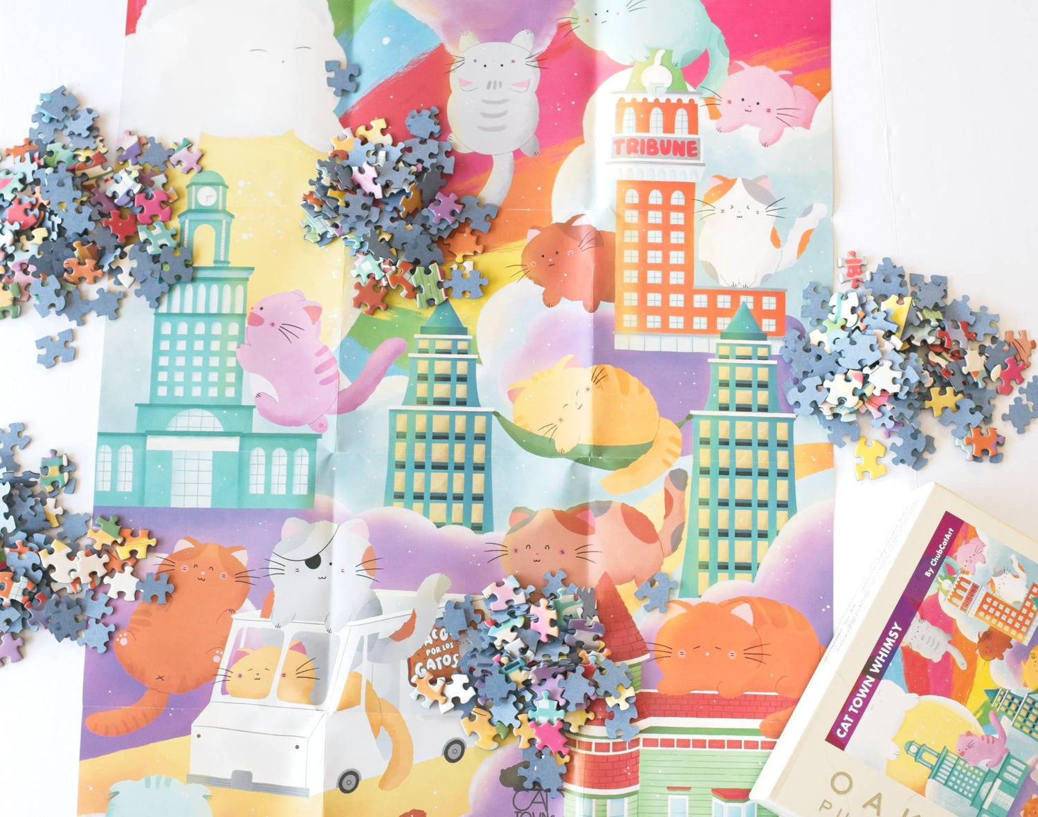 Colorful poster with cartoon animals and Oakland, CA buildings and puzzle pieces with blue backing scattered around in piles. the top of the puzzle box is visible in the corner labeled "Cat Town Whimsy"