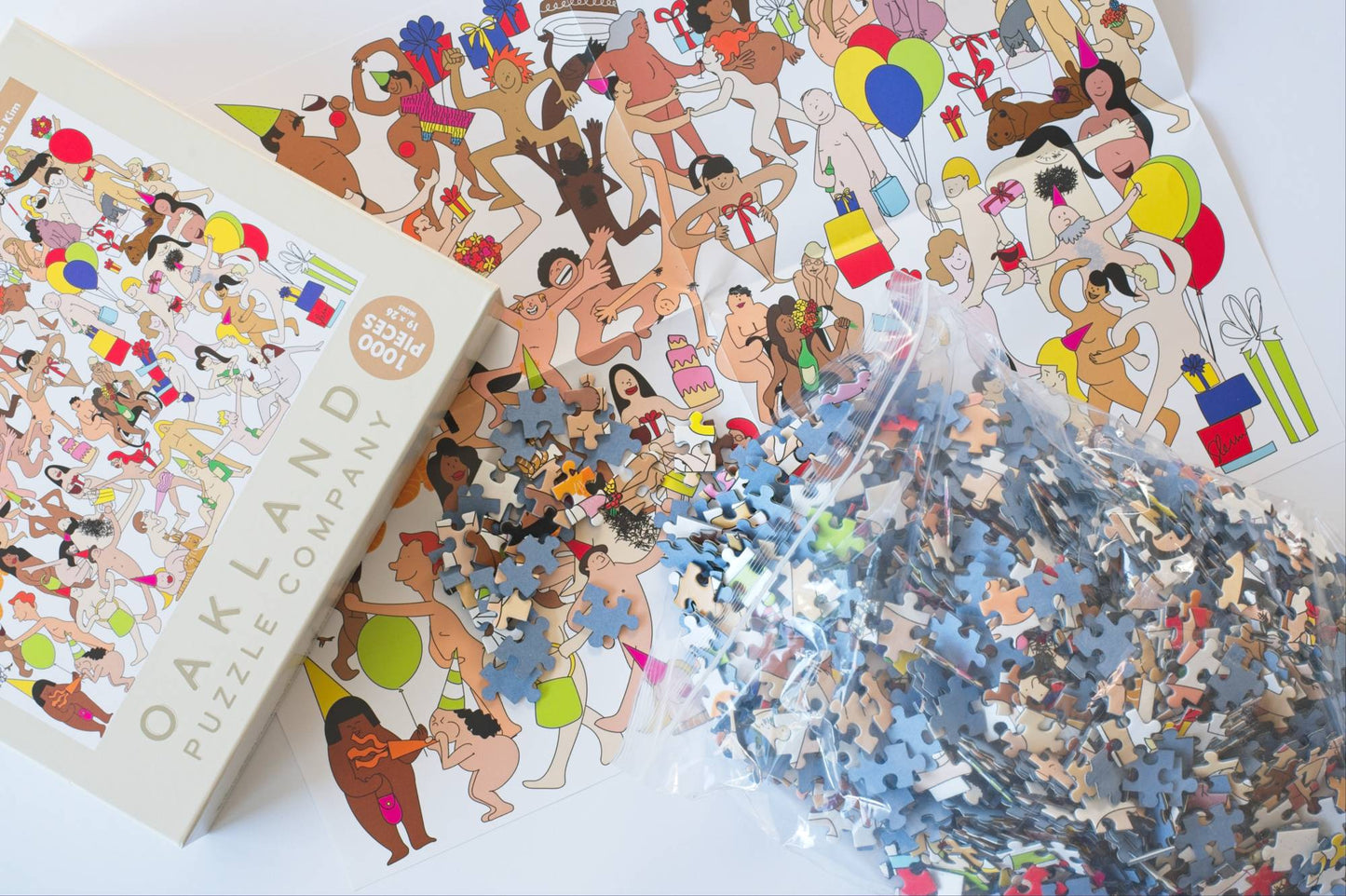 Jigsaw puzzle pieces spilling out of a resealable plastic bag onto a colorful puzzle image next to a branded Oakland Puzzle Company box