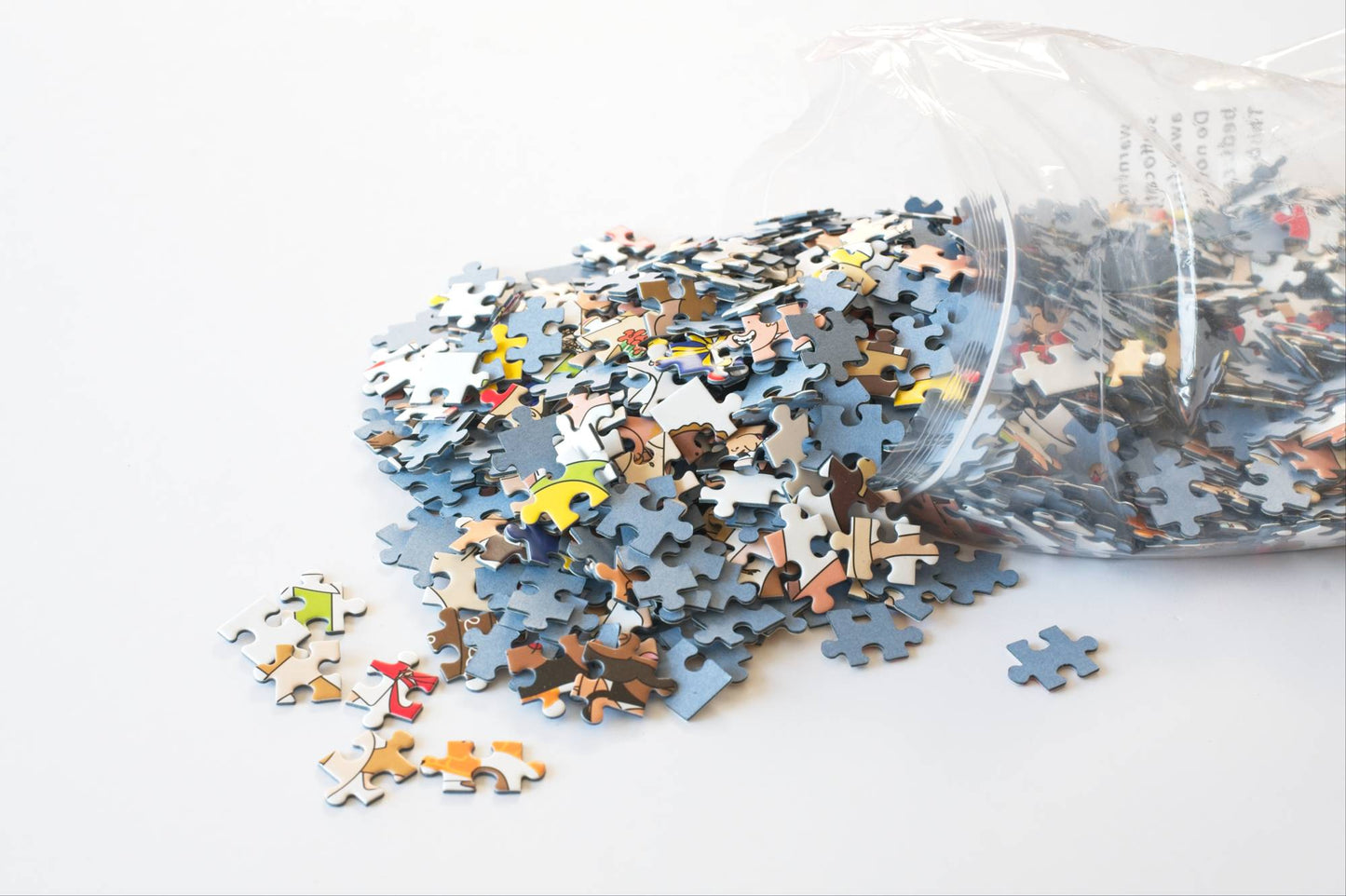 Jigsaw puzzle pieces spilling out of a clear plastic bag on a white background