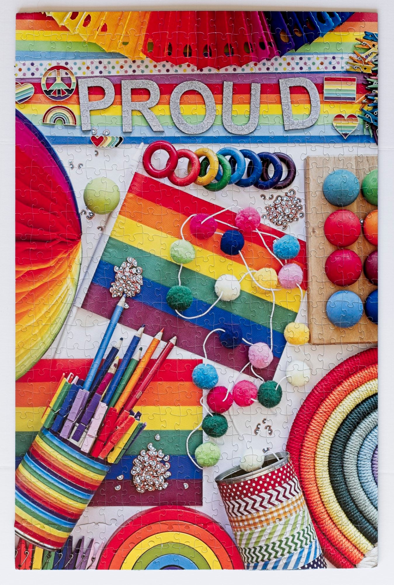 A photo of a completed jigsaw puzzle that features a variety of both organized and messy rainbow-themed items with the word Proud on the top.