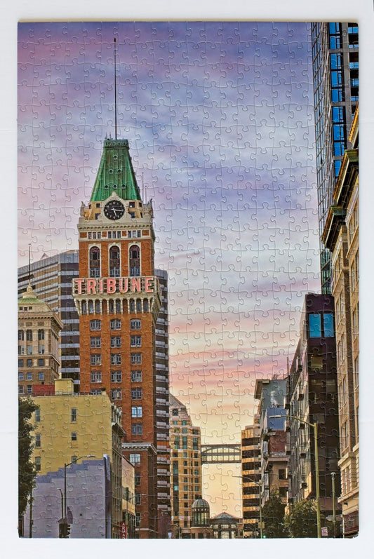A completed jigsaw puzzle showing the Tribune Tower and surrounding buildings. The  sky shows a sunset gradient and a walkway between buildings is visible.