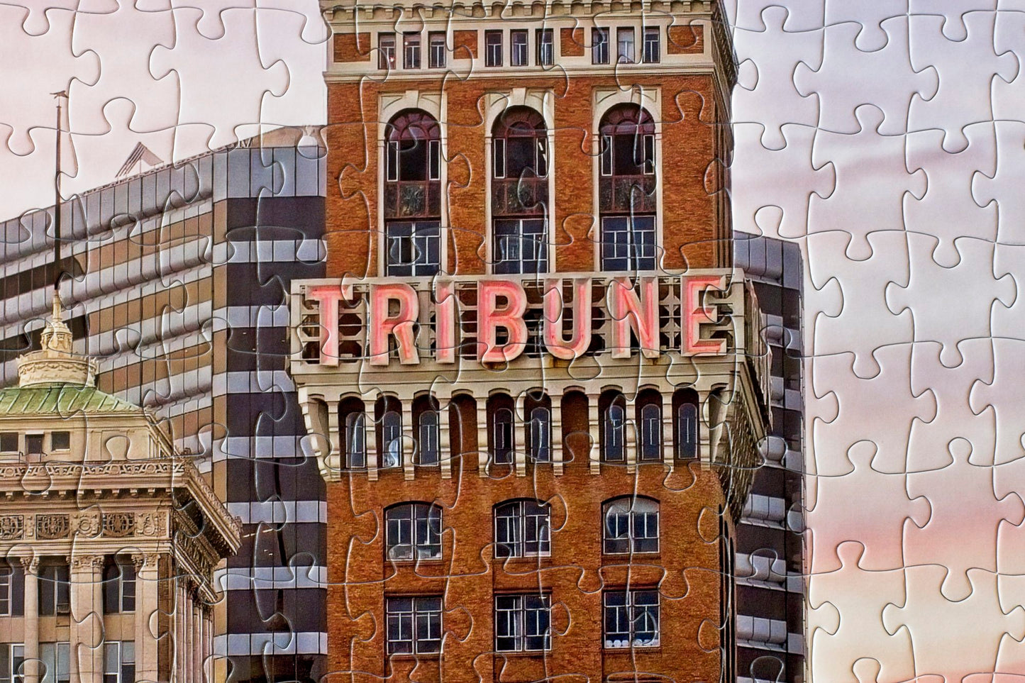 A close-up of the completed Tribune Tower jigsaw puzzle with the Tribune name centered in the image with a few other buildings and a purplish sky behind.