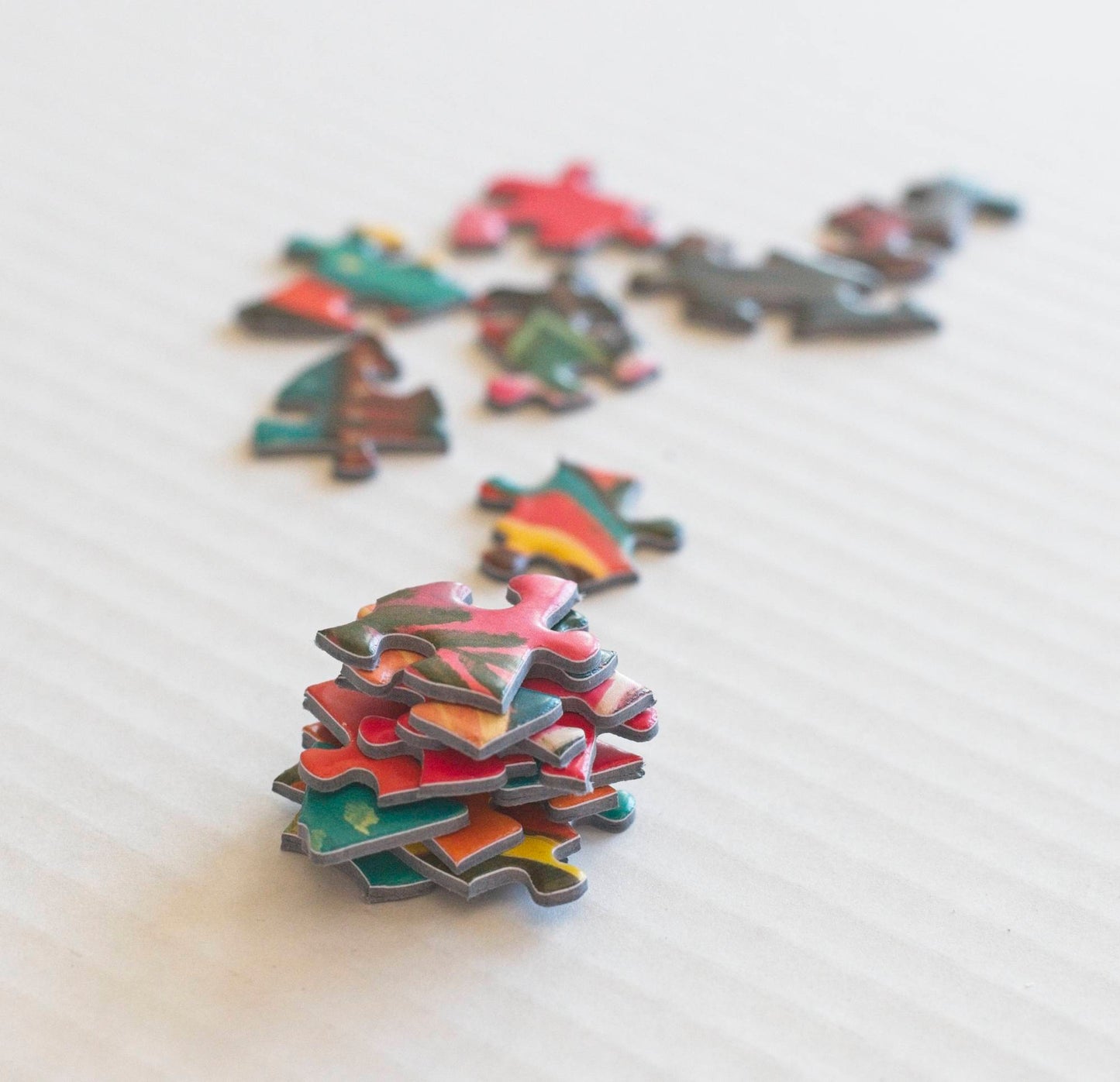 A stack of sturdy and colorful random shaped puzzle pieces with other scattered pieces out of focus in the background