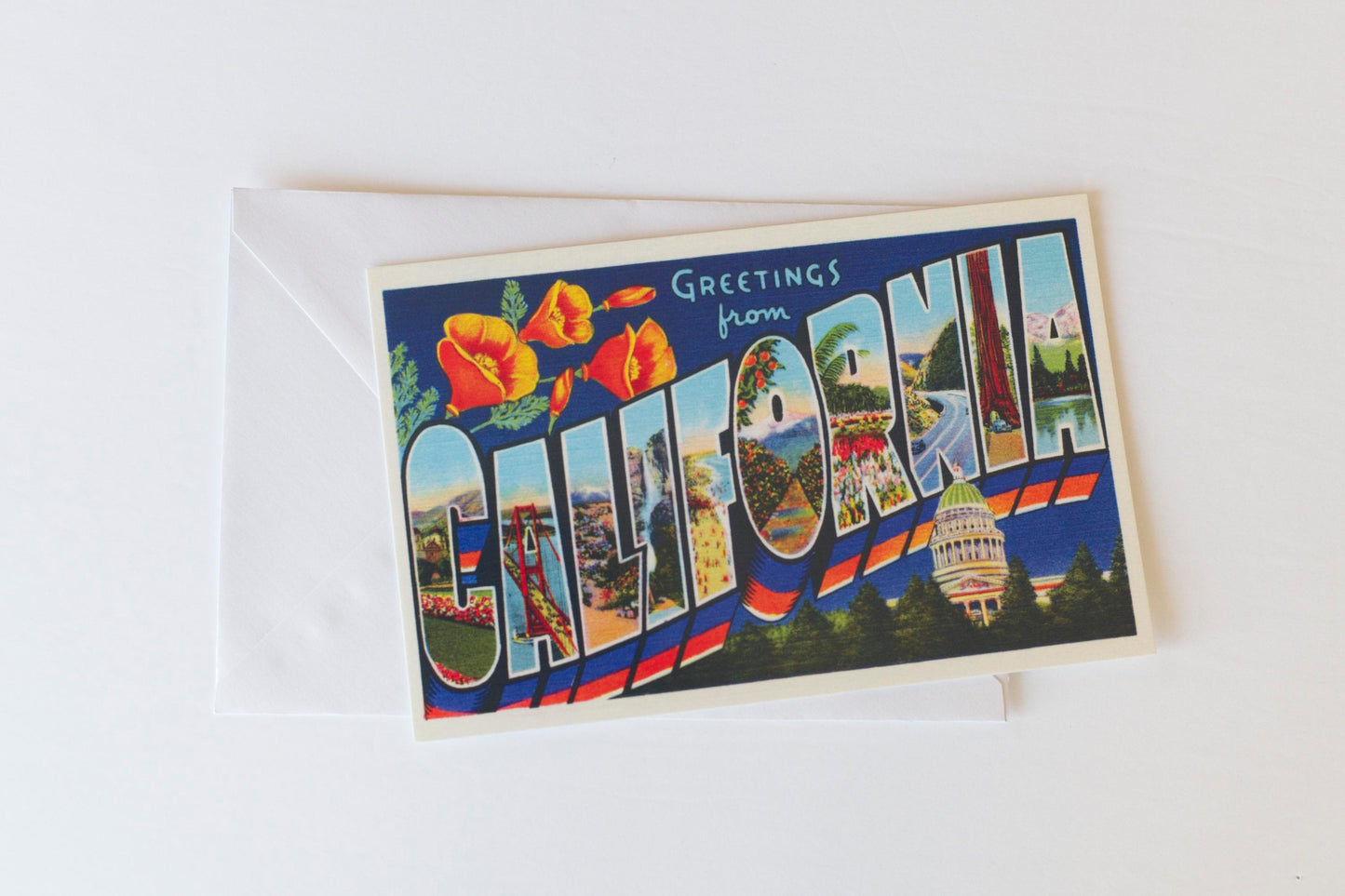 A photo of a vintage postcard with Greetings from California printed in large letters filled with images resting on a white envelope on a white background