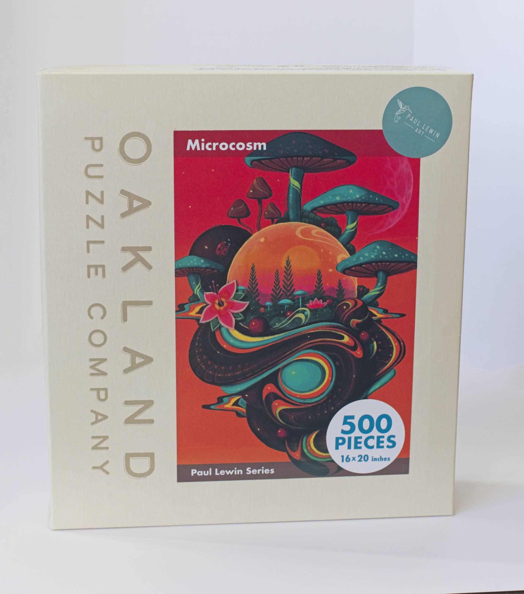 A box branded Oakland Puzzle Company with a colorful orange Afrofuturist image with mushrooms, flowers, and orbs titled Microcosm Paul Lewin Series