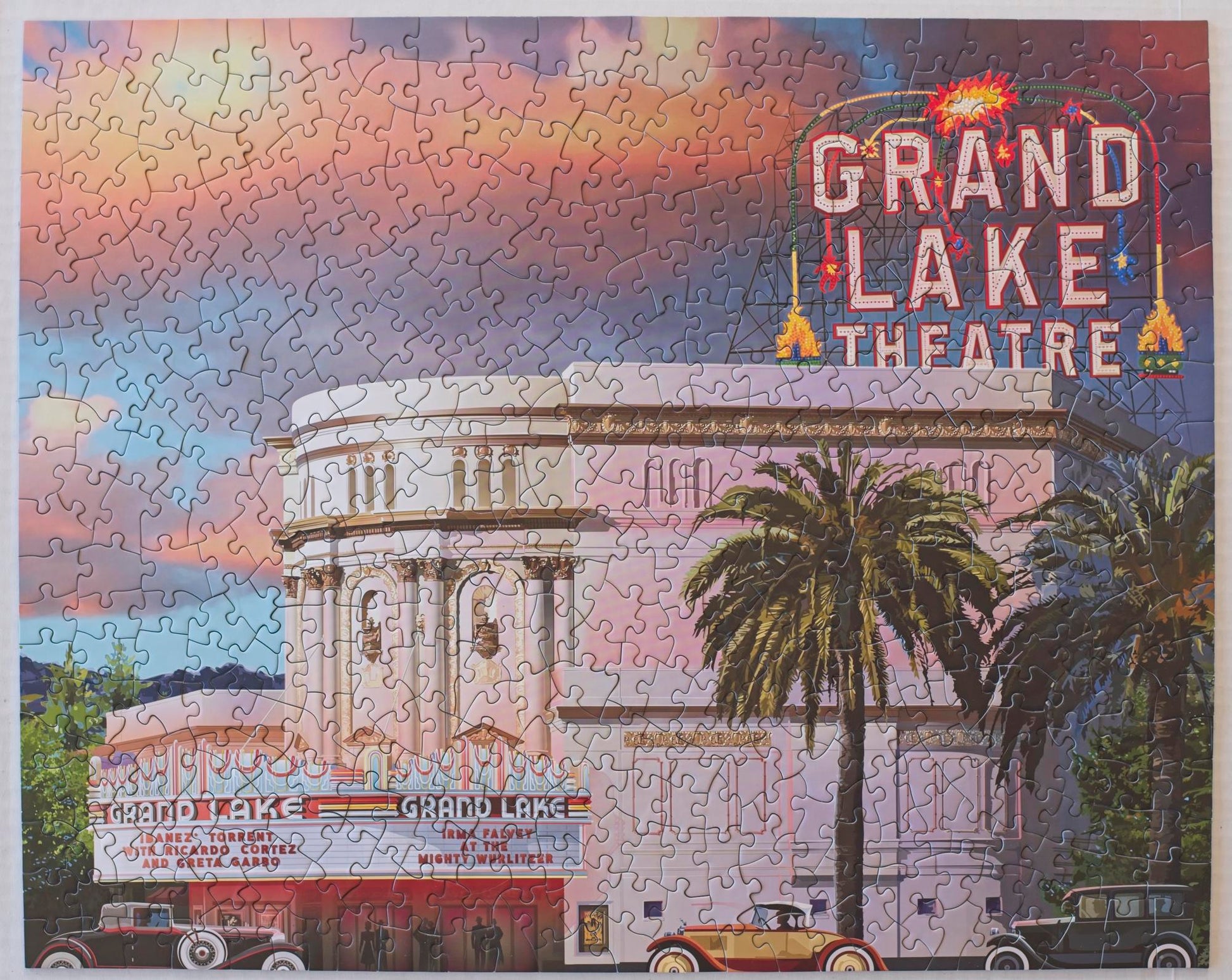 A completed jigsaw puzzle featuring an illustration of the Grand Lake Theatre with a moody sky and classic cars in front.
