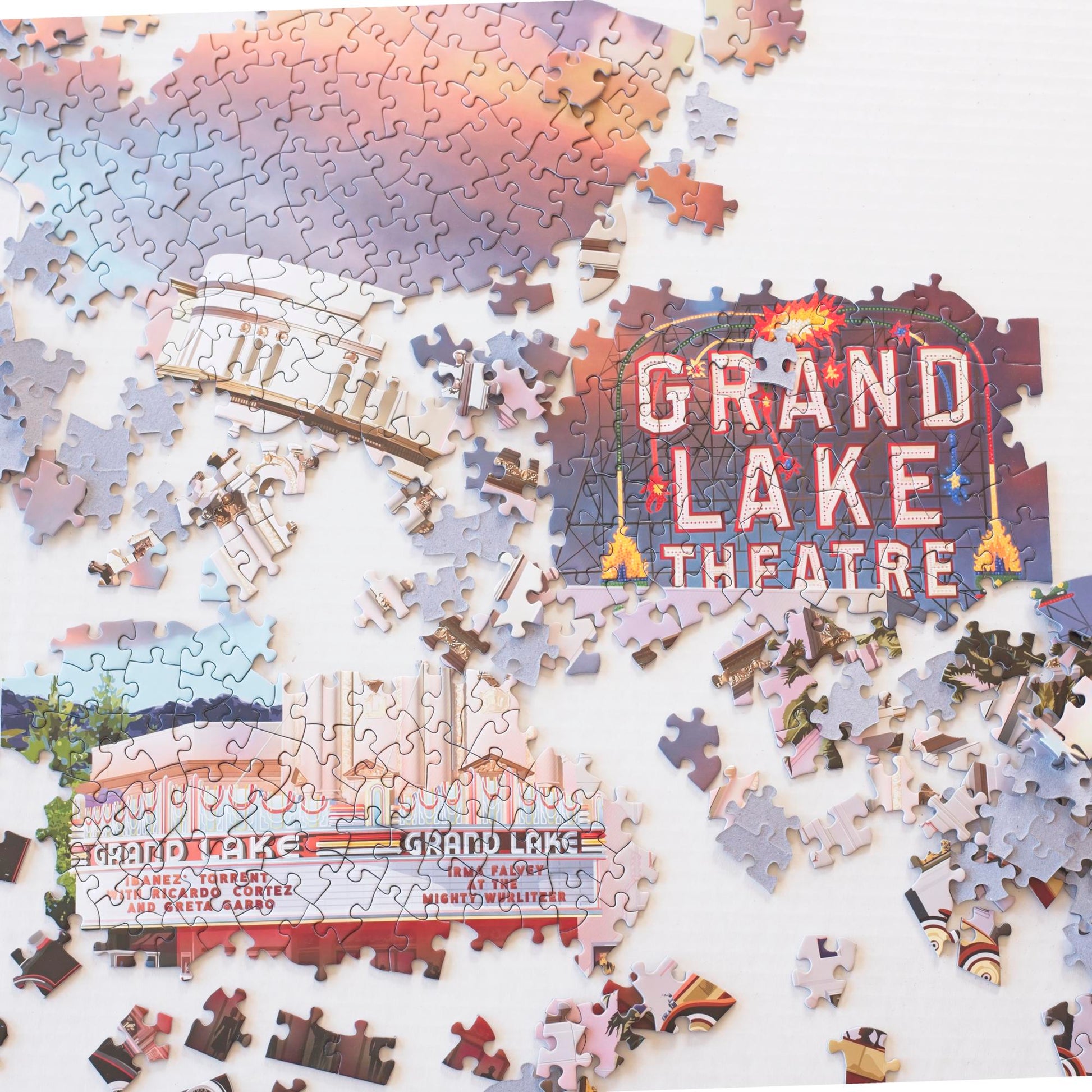 several sections of partially assembled puzzles including the Grand Lake Theatre sign and marquee with puzzle pieces scattered around