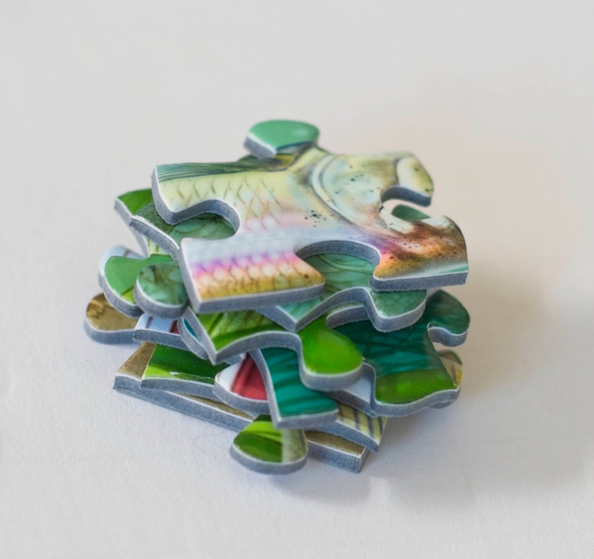 A close up of a  stack of colorful jigsaw puzzle pieces with a piece on top that looks like scales of a rainbow trout