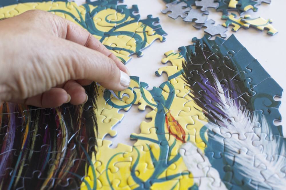 A hand placing a bright blue and yellow puzzle piece into a partially completed puzzle.
