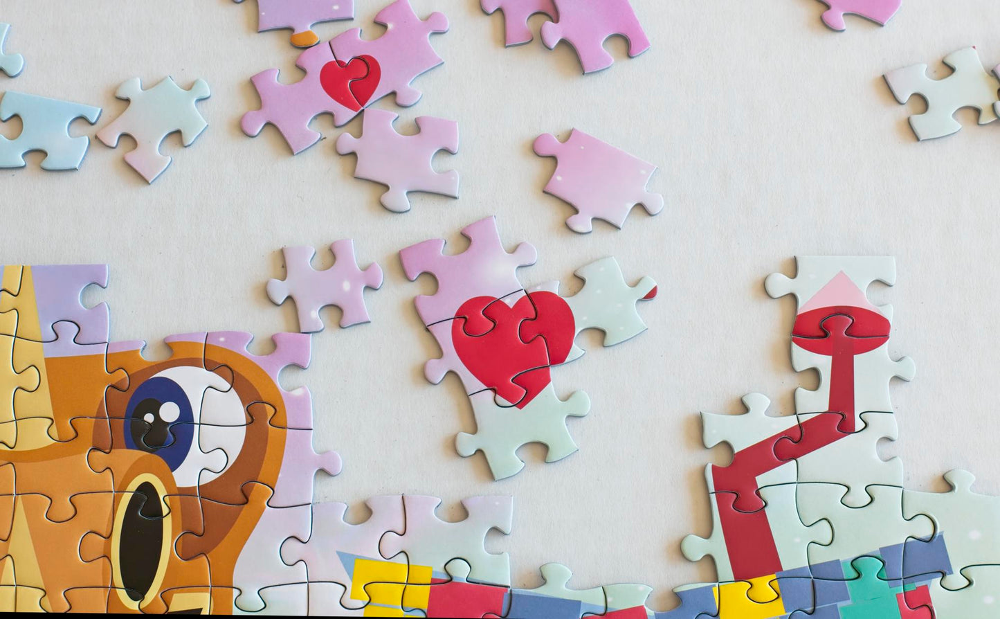 A close up photo of some conjoined puzzle pieces showing a dragons eye, hearts, and a crooked stovepipe with scattered pieces above them.