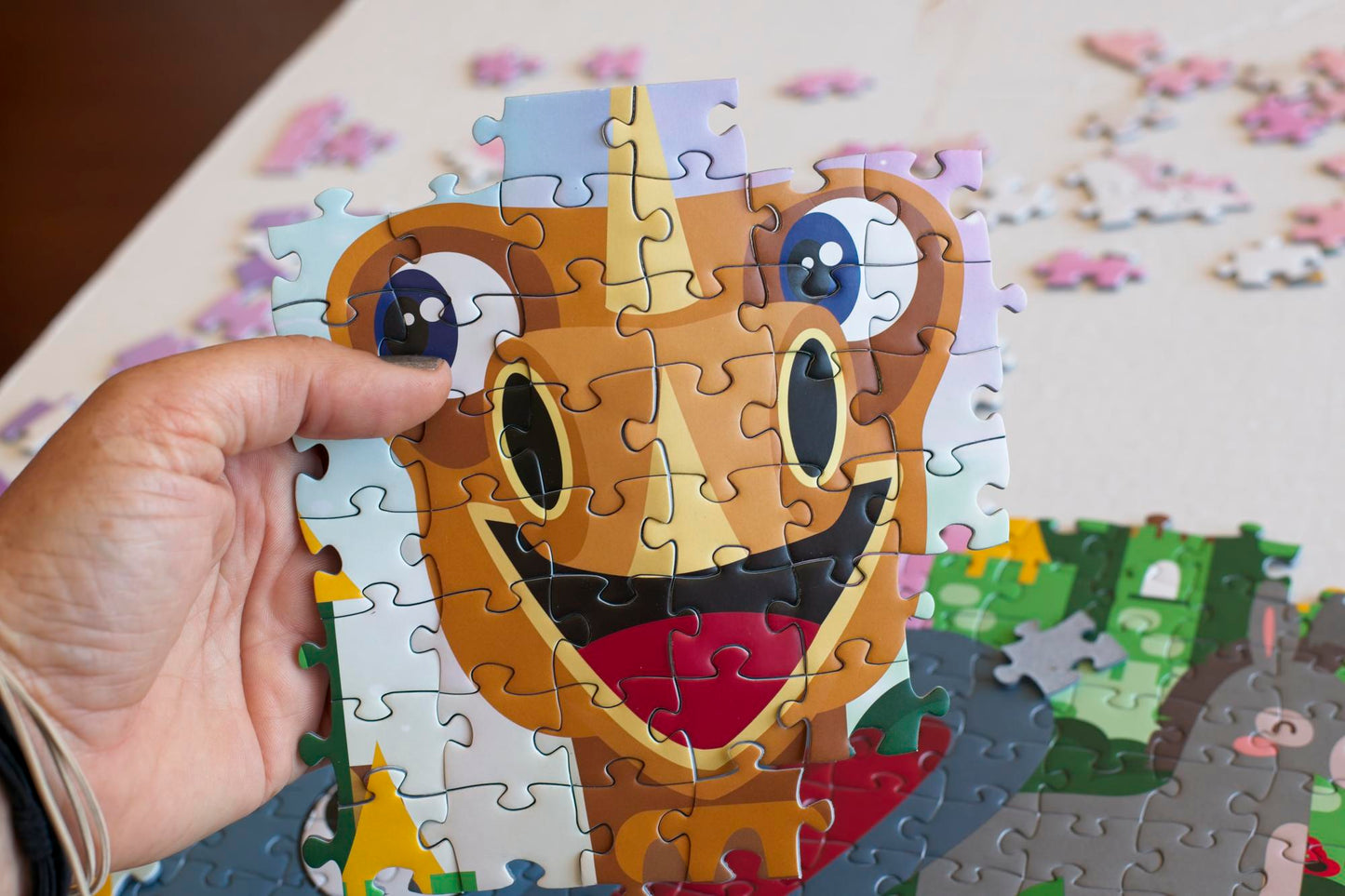 A hand holding conjoined puzzle pieces with an illustrated dragon with a completed puzzle and strewn pieces in the backgrouns.