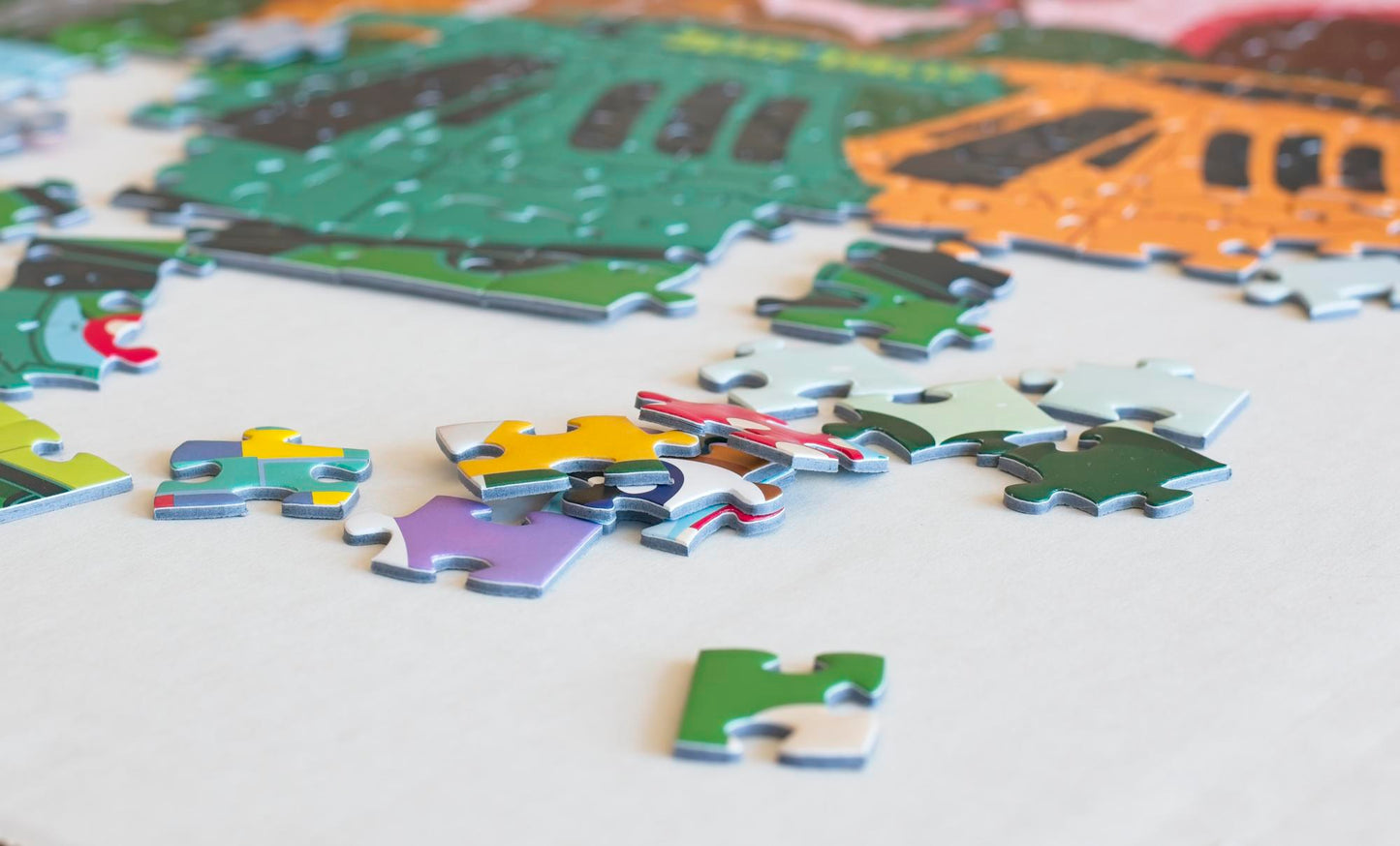 A stack of puzzle pieces with some strewn nearby with a partially completed colorful illustrated puzzle in the background.