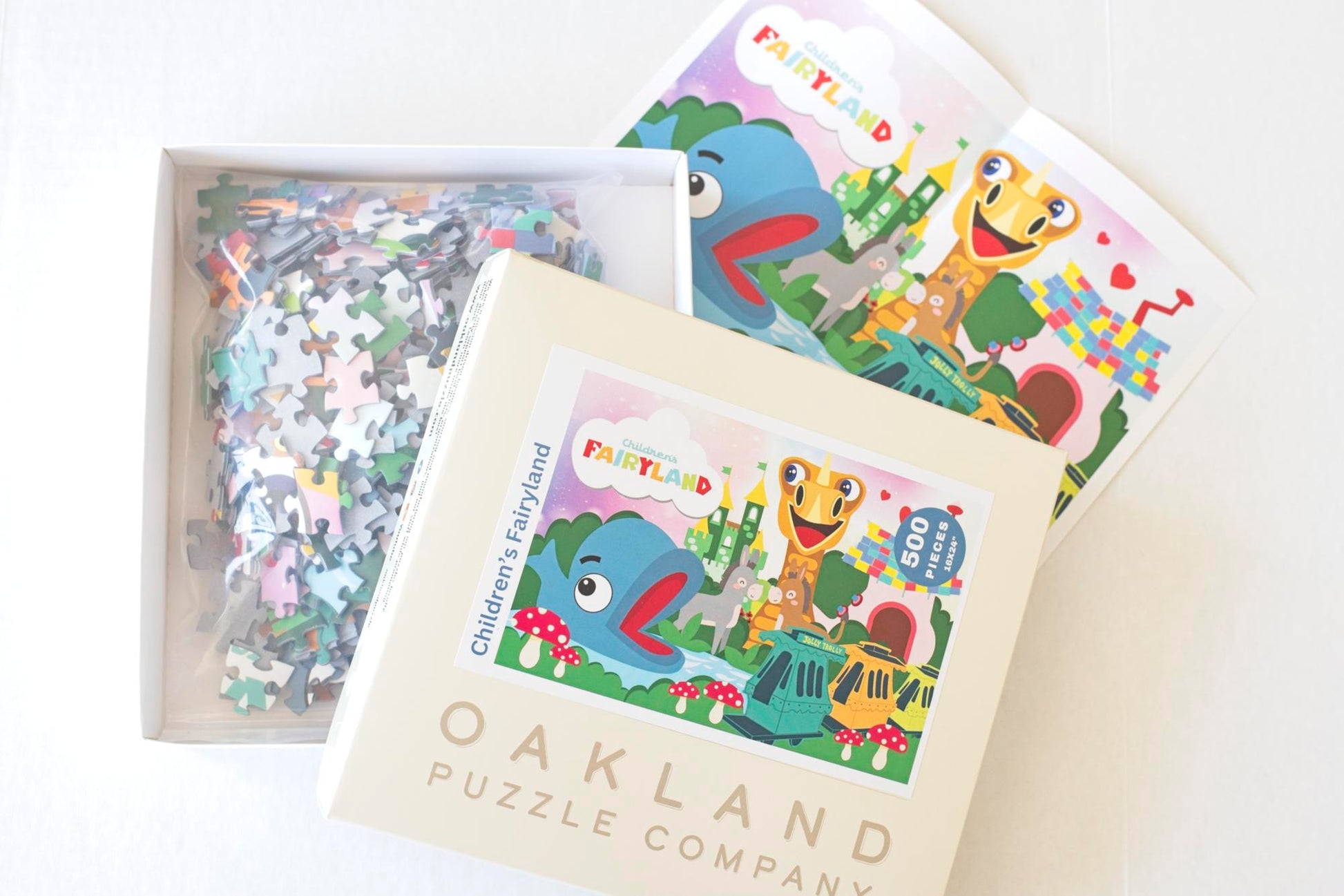 An opened box featuring the Children's Fairyland puzzle exposing colorful jigsaw puzzle pieces in a resealable plastic bag with a puzzle poster next to it.