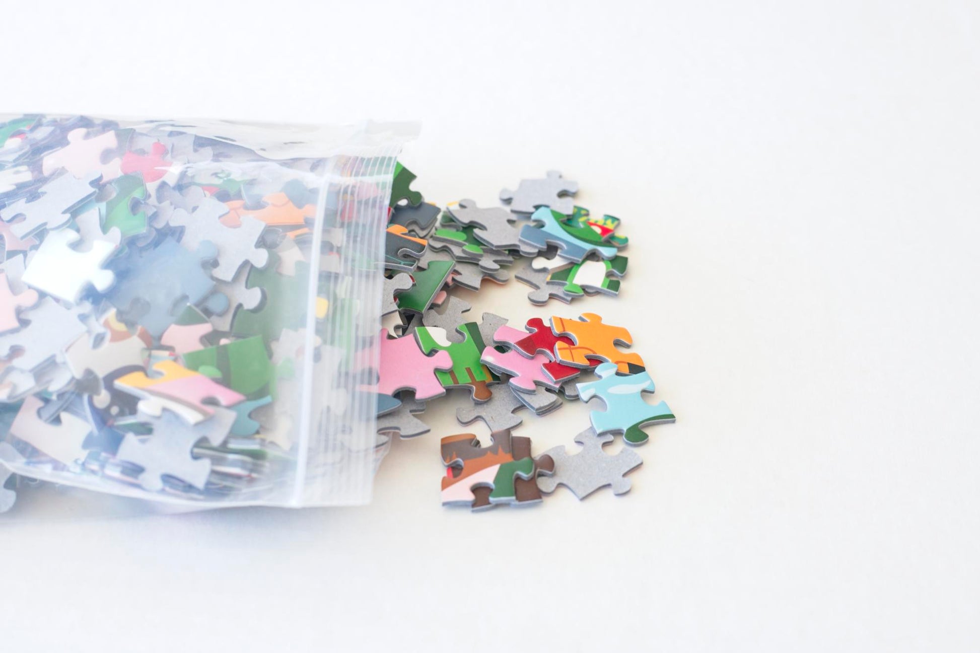 The end of a resealable plastic bag with colorful puzzle pieces spilling from it.