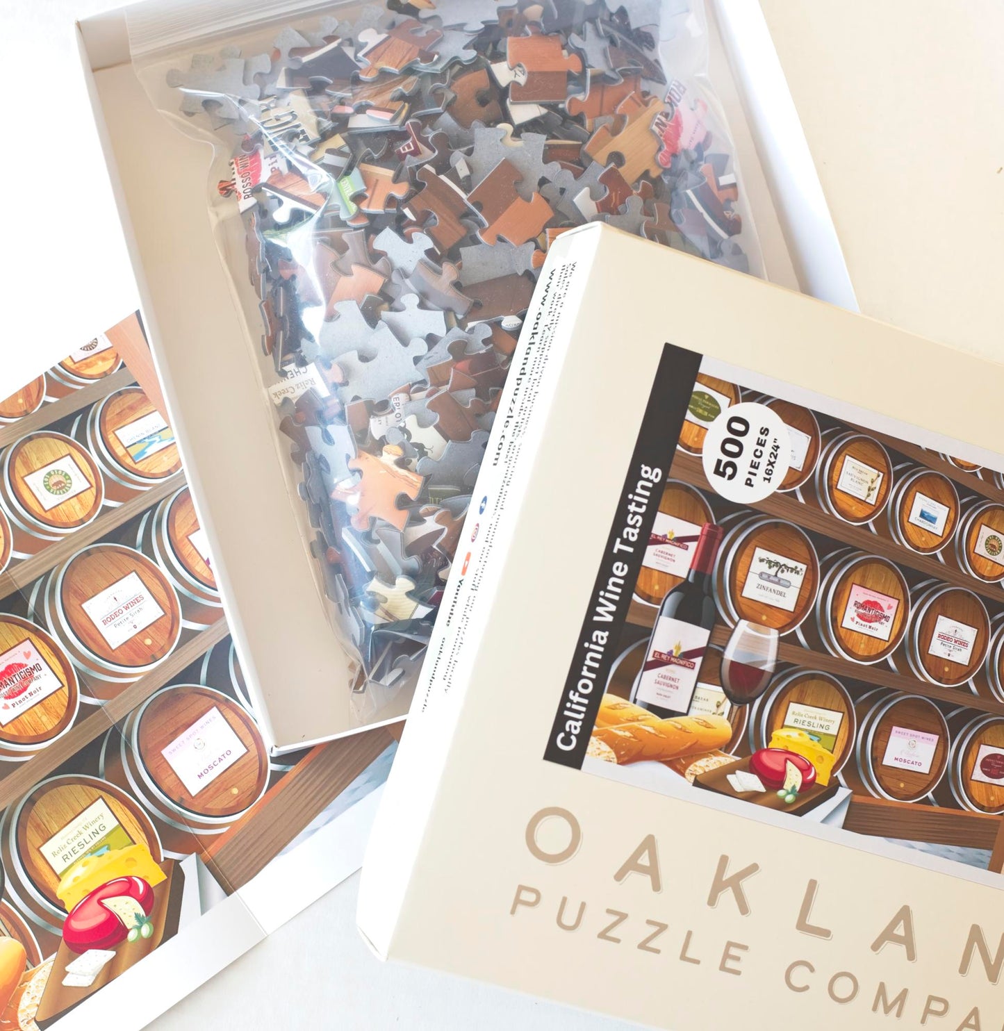 A close up of an opened box of the Oakland Puzzle Company California Wine Tasting jigsaw puzzle. Inside the box is a resealable back with jigsaw puzzle pieces and behind the box is a puzzle poster.