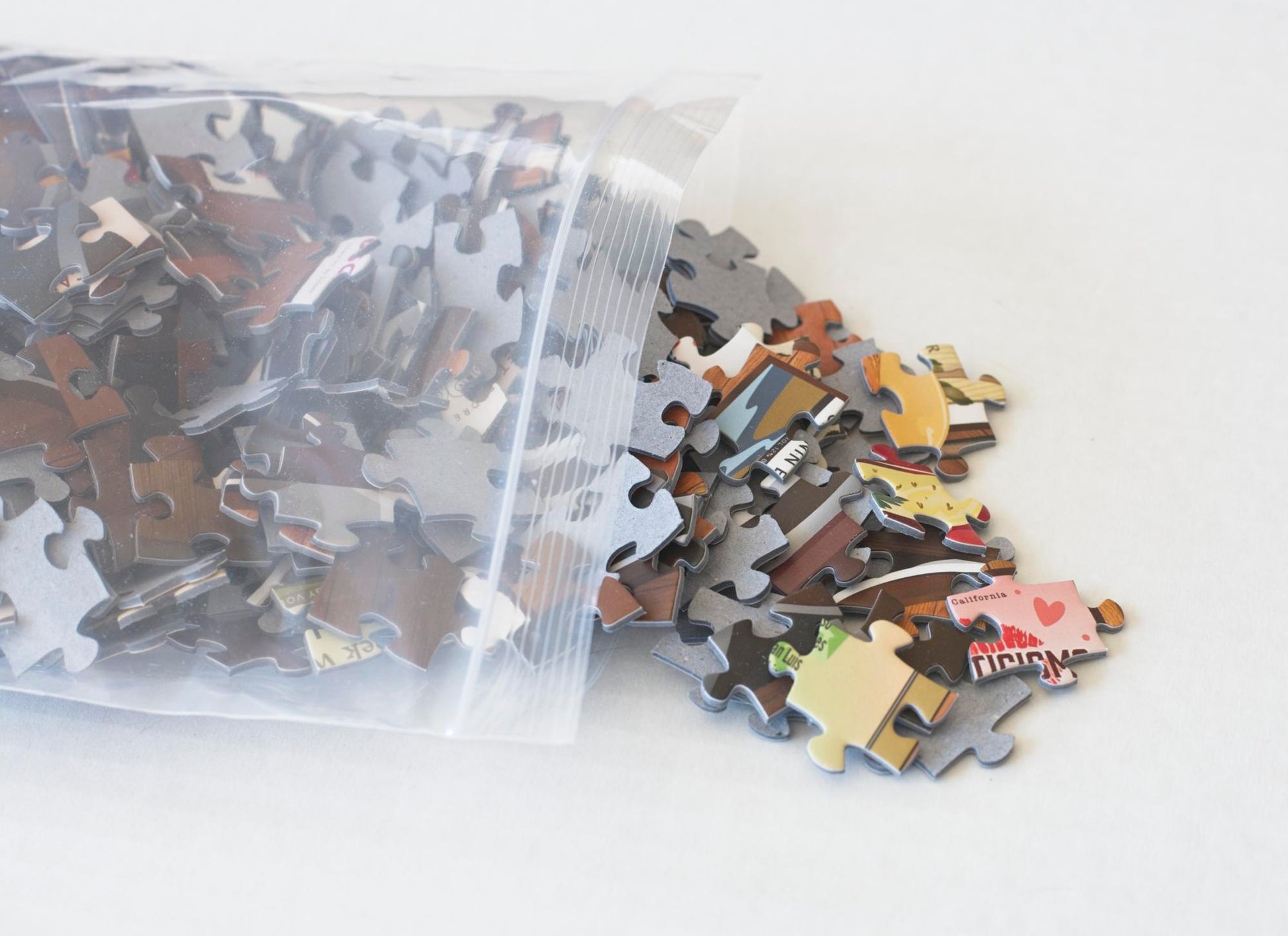 A resealable plastic bag with colorful jigsaw puzzle pieces spilling from it.