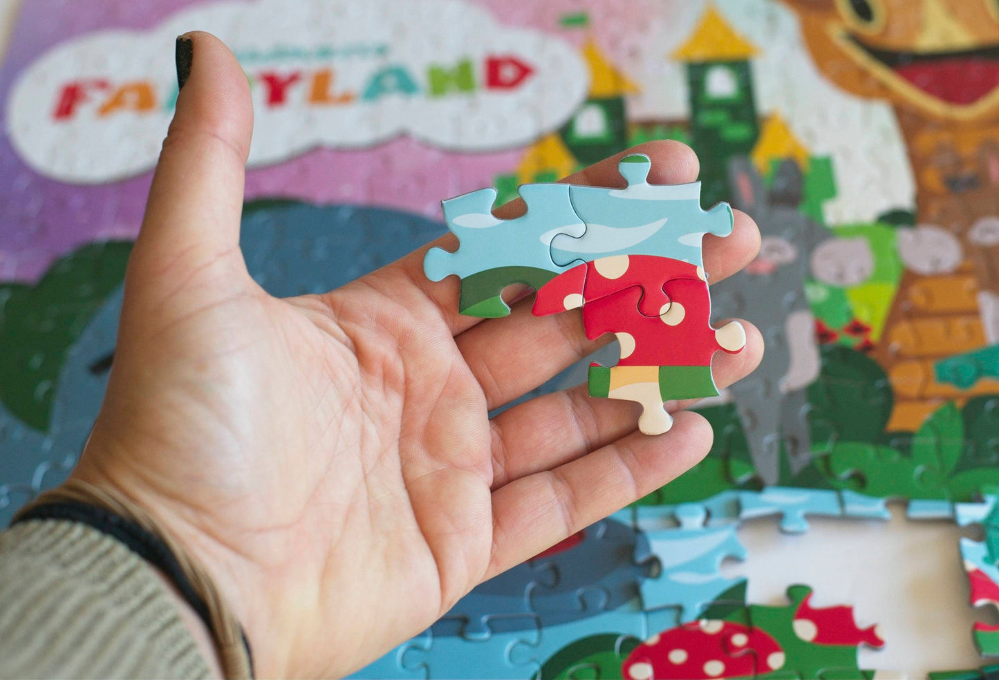 A hand holding three large joined puzzle pieces showing a red mushroom with spots and water.