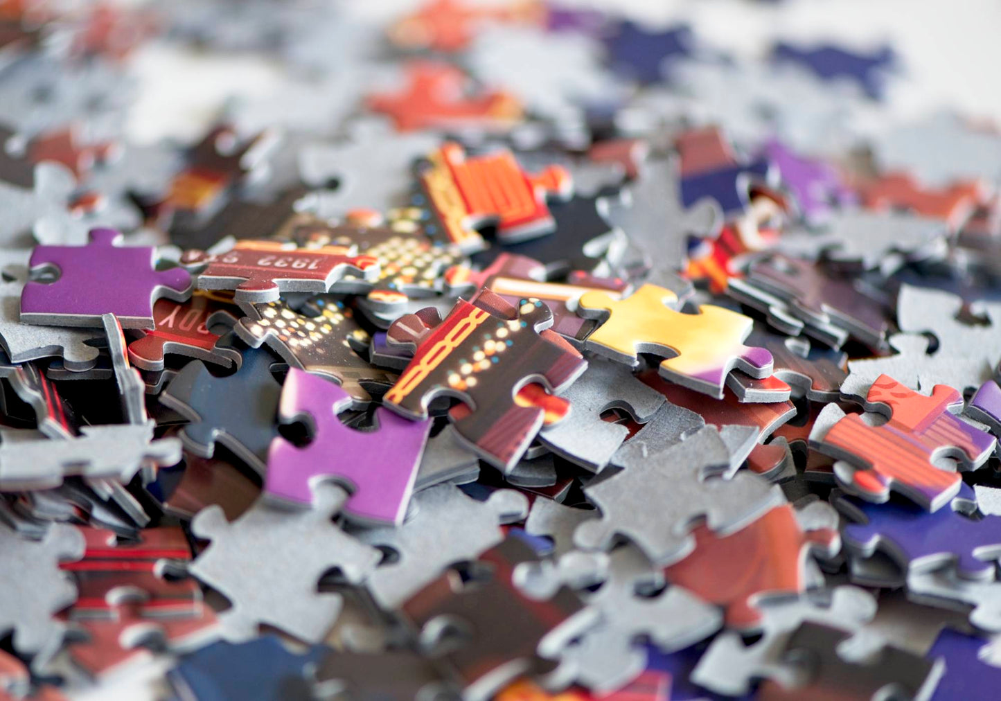 A large pile of randomly strewn jigsaw puzzle pieces showing out of focus lights, stripes, and solids with red, yellow, blue, and purple tones