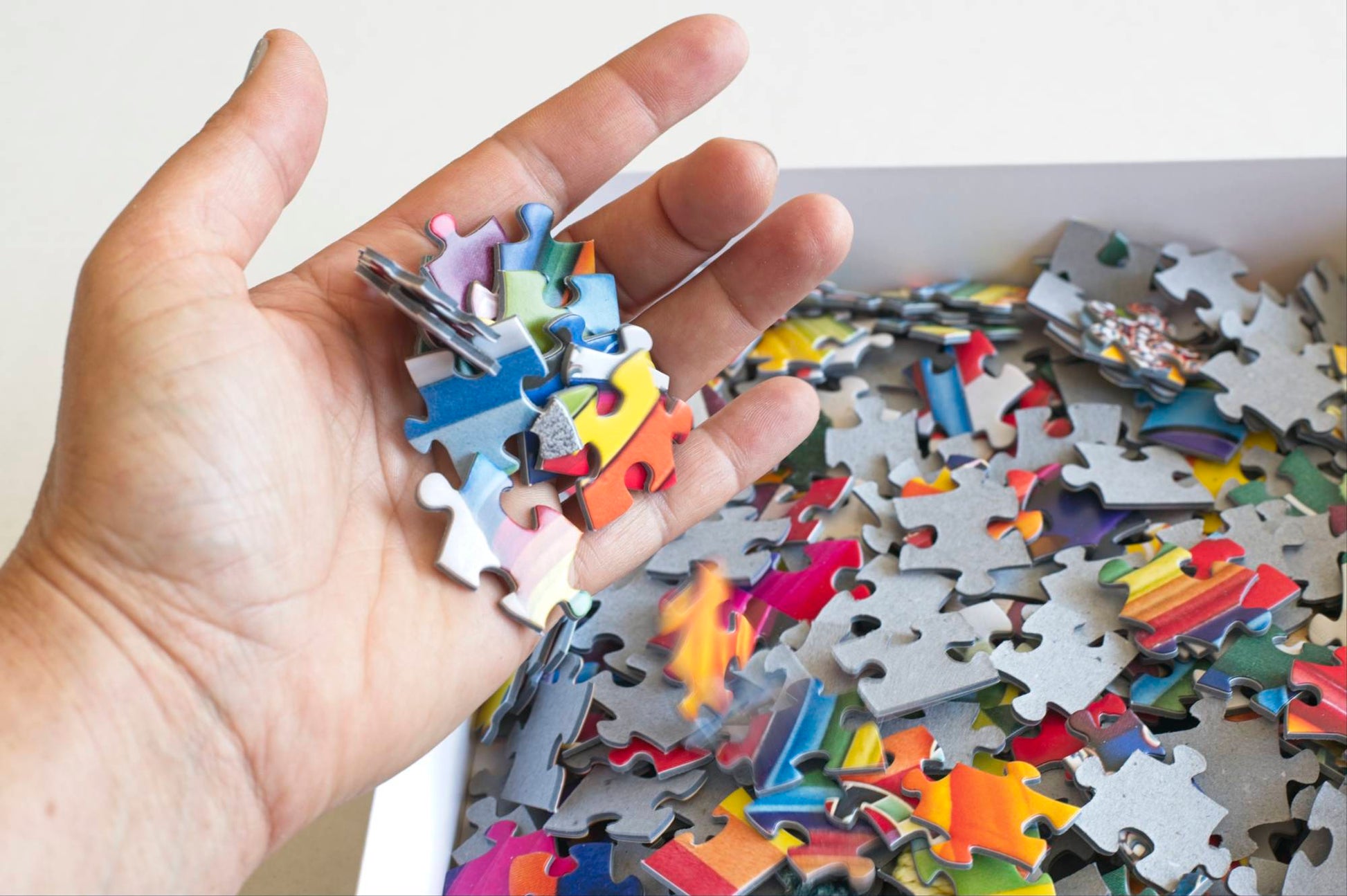 Hand holding a colorful puzzle piece above a pile of assorted puzzle pieces.