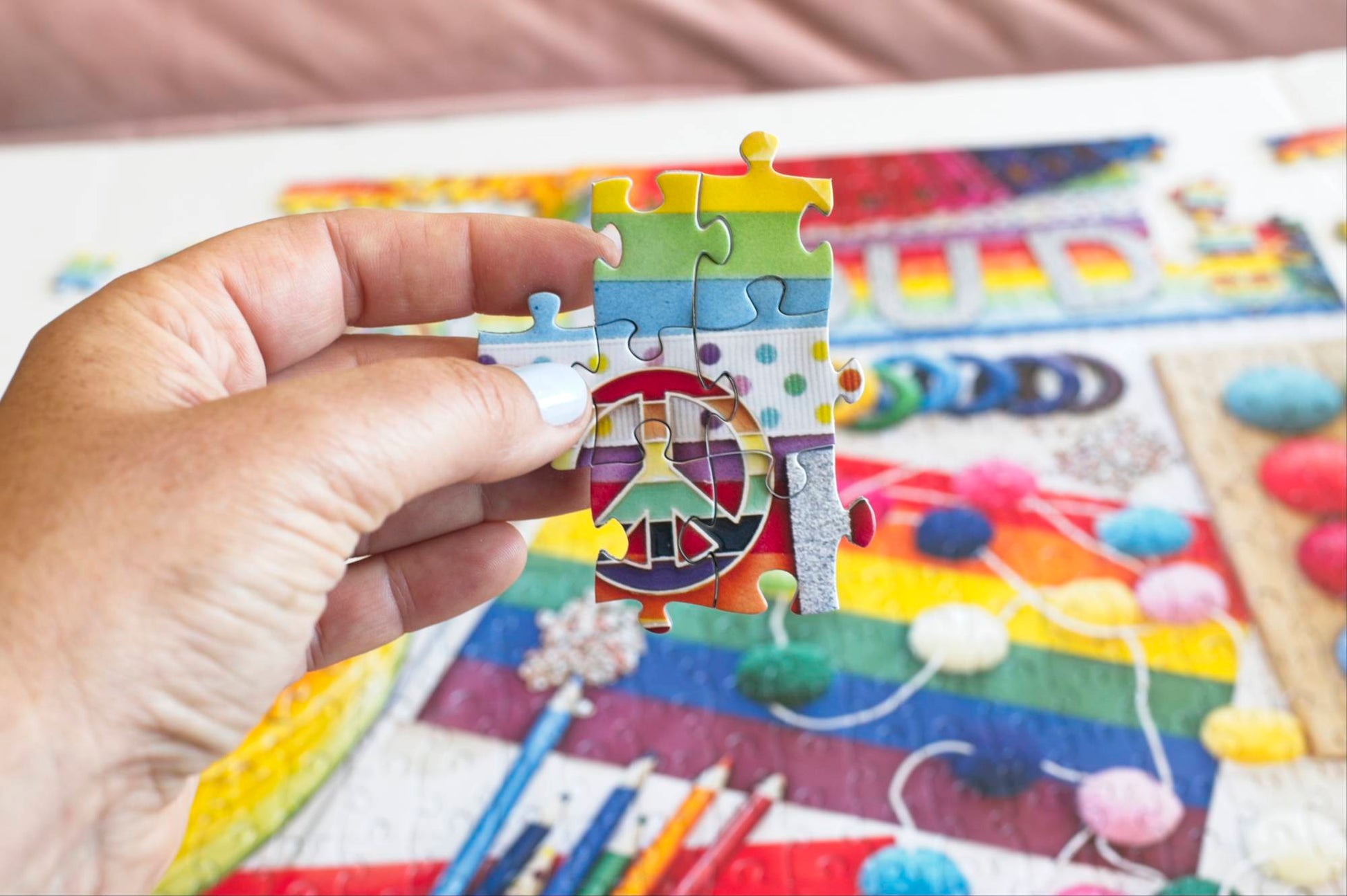 A hand holding a section of a colorful puzzle section held over a partially completed puzzle in the background.
