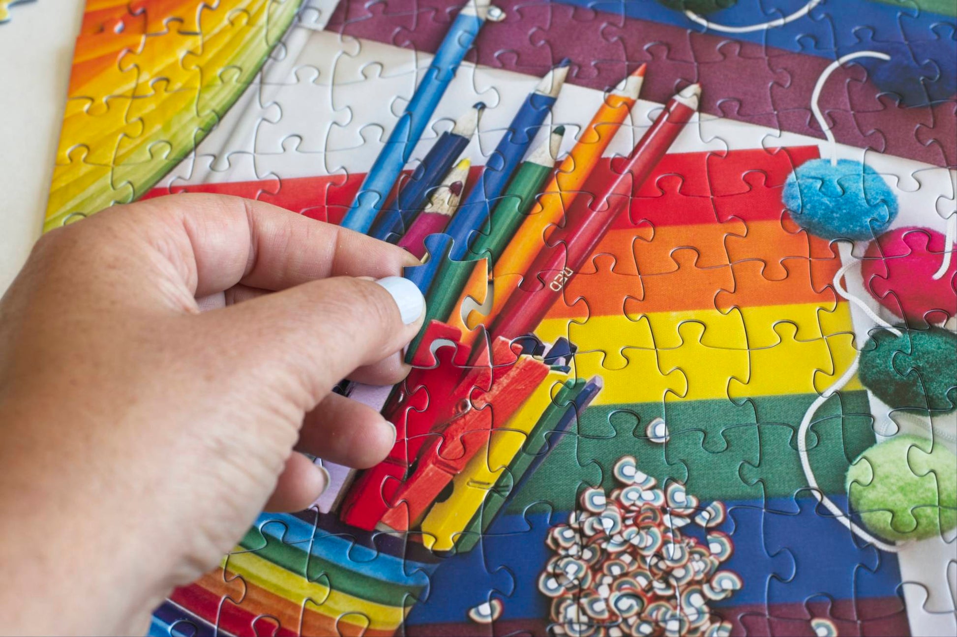 Colorful puzzle with rainbow themed items like flags and pencils and a hand interacting with it.