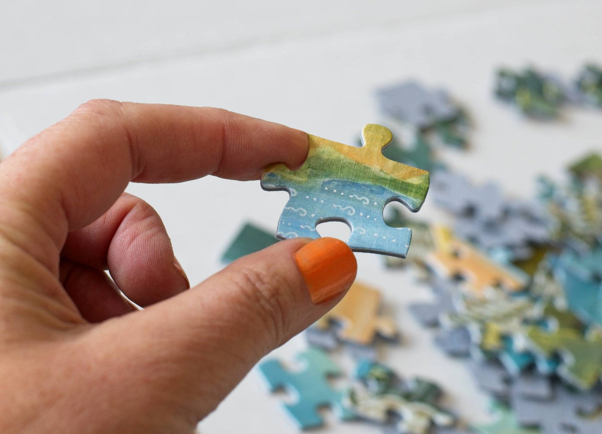 Hand holding a large puzzle piece with scattered puzzle pieces in the background