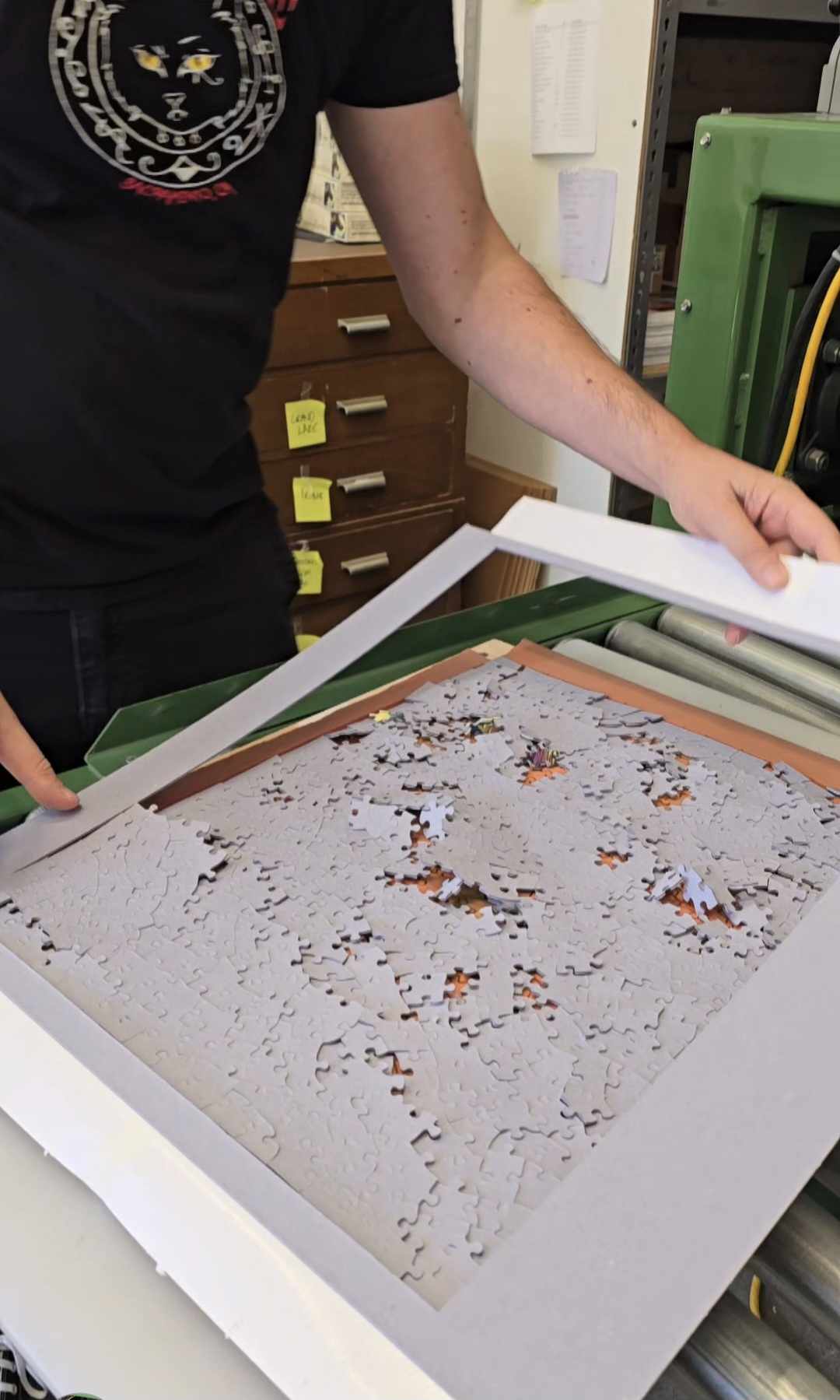 A person pulling off the excess frame from a cut jigsaw puzzle being removed from a puzzle die