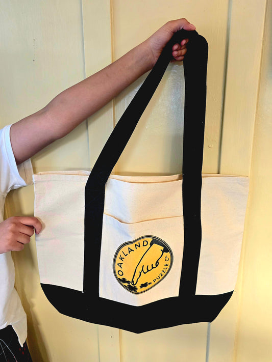 Person holding a beige tote bag with a logo against a light-colored wall