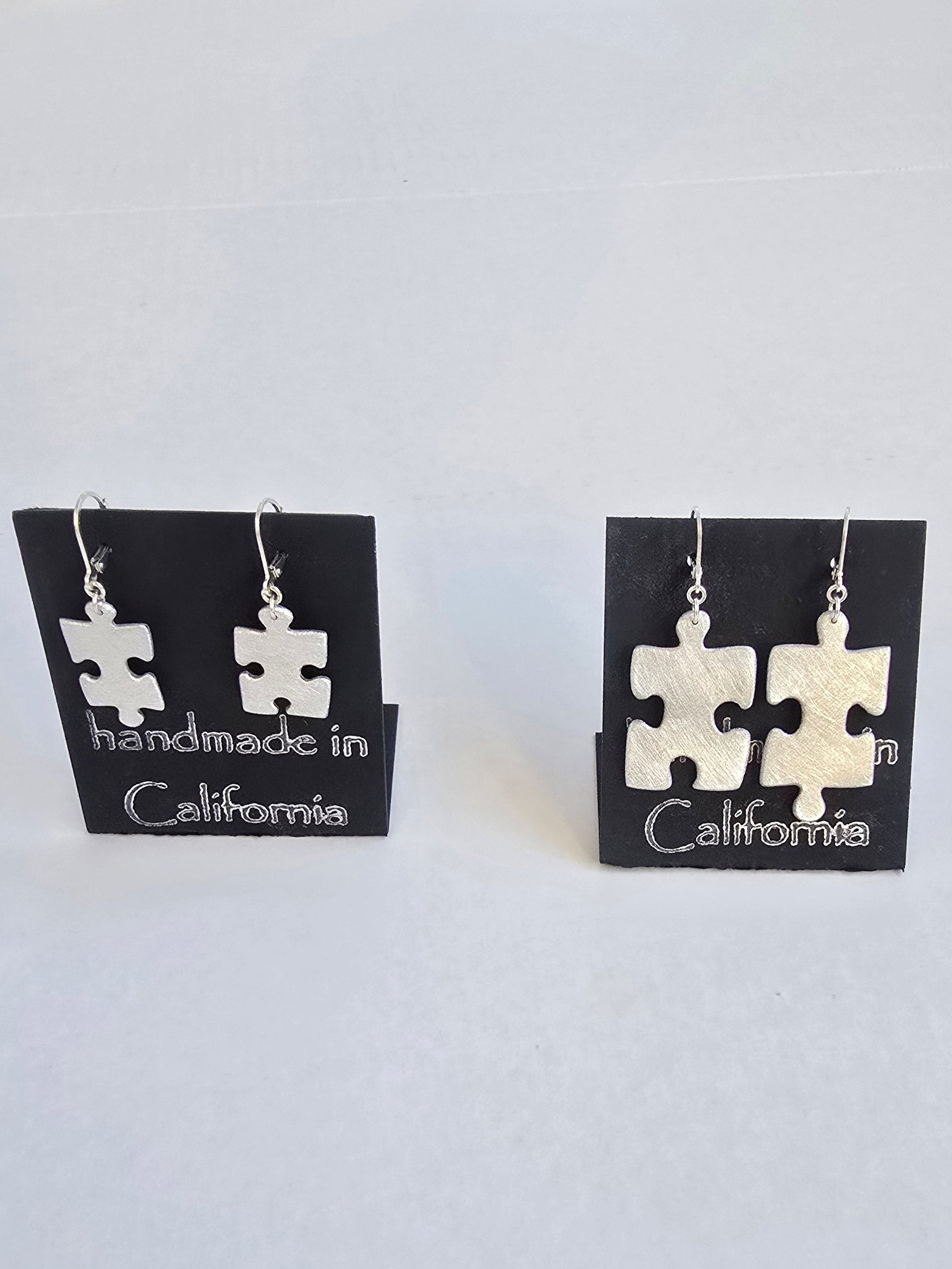 Pair of puzzle piece earrings on a card with 'handmade in California' text, against a white background.