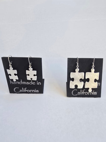 Pair of puzzle piece earrings on a card with 'handmade in California' text, against a white background.