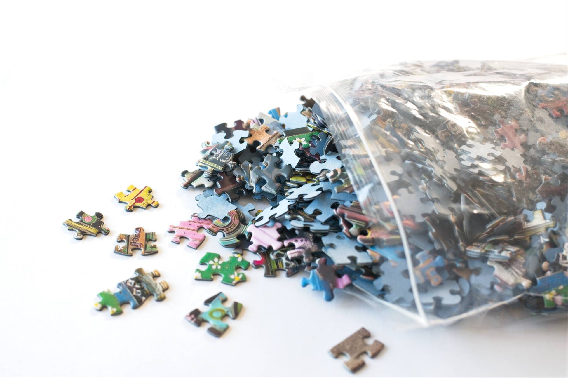 Pile of puzzle pieces spilling out of a resealable plastic bag on a white background