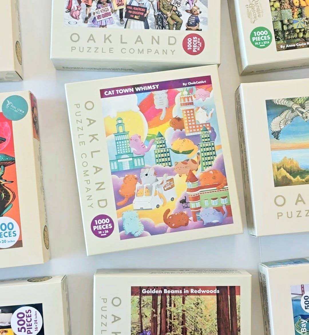 A flatlay photo of a variety of colorful jigsaw puzzles labeled Oakland Puzzle Company