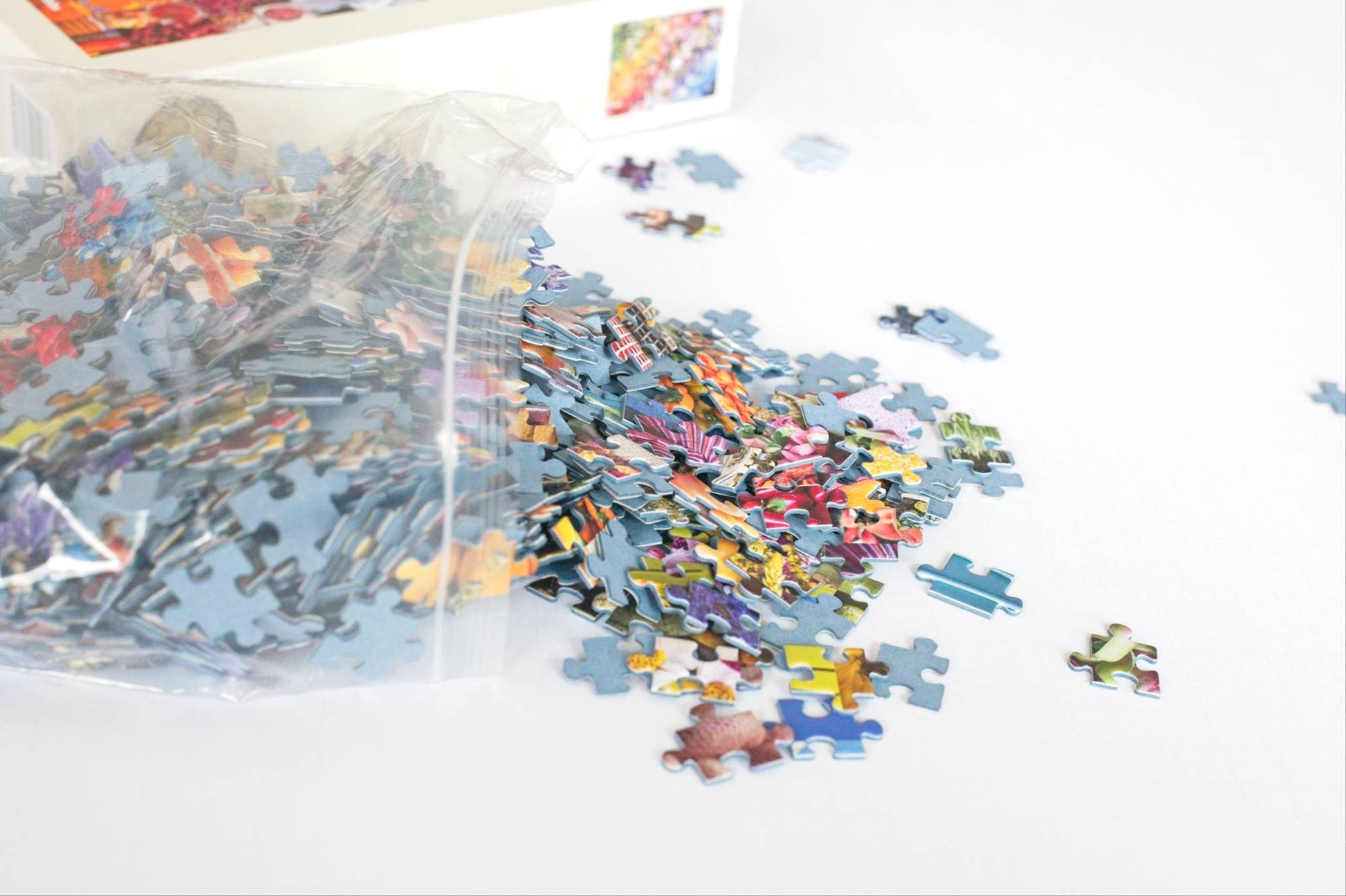 Colorful puzzle pieces spilling out of a resealable plastic bag with an out of focus box in the background.