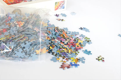 Colorful puzzle pieces spilling out of a resealable plastic bag with an out of focus box in the background.