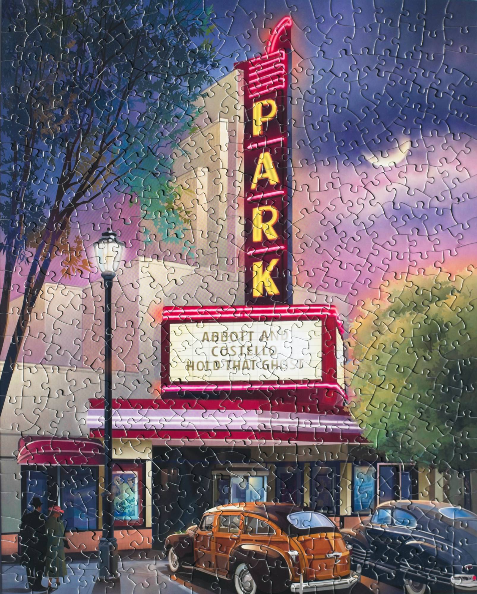 A completed jigsaw puzzle featuring a colorful night skay and a neon sign on a historic theater reading "Park" with cars parked below