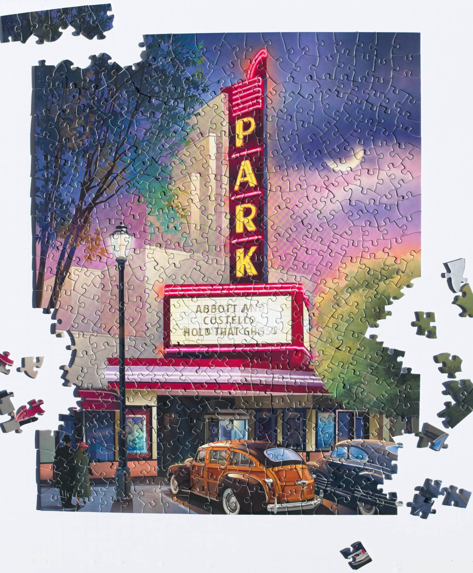 Jigsaw puzzle with a completed section and scattered pieces showing a  classic theater with a neon sign at night.